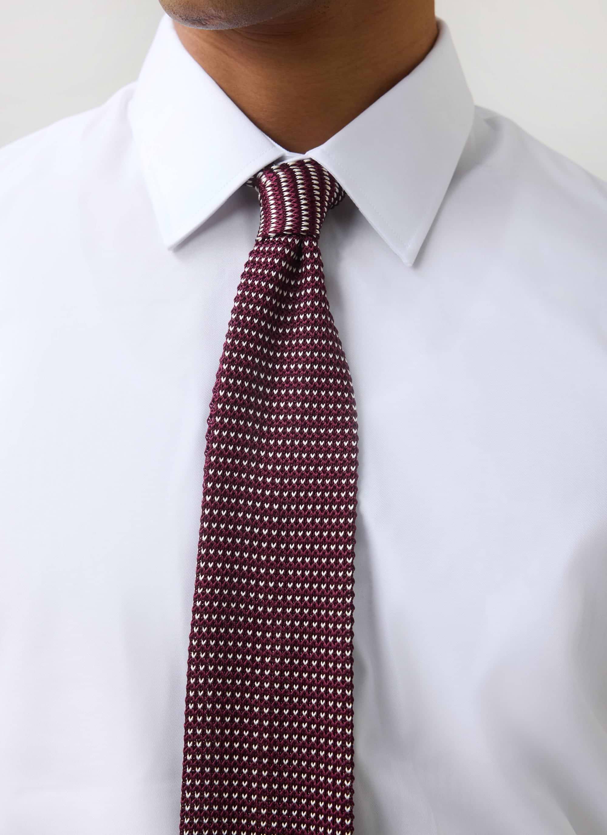 Close-up of a model wearing the Percival Birdseye Silk Tie in red, showing the detailed knit texture against a white shirt.