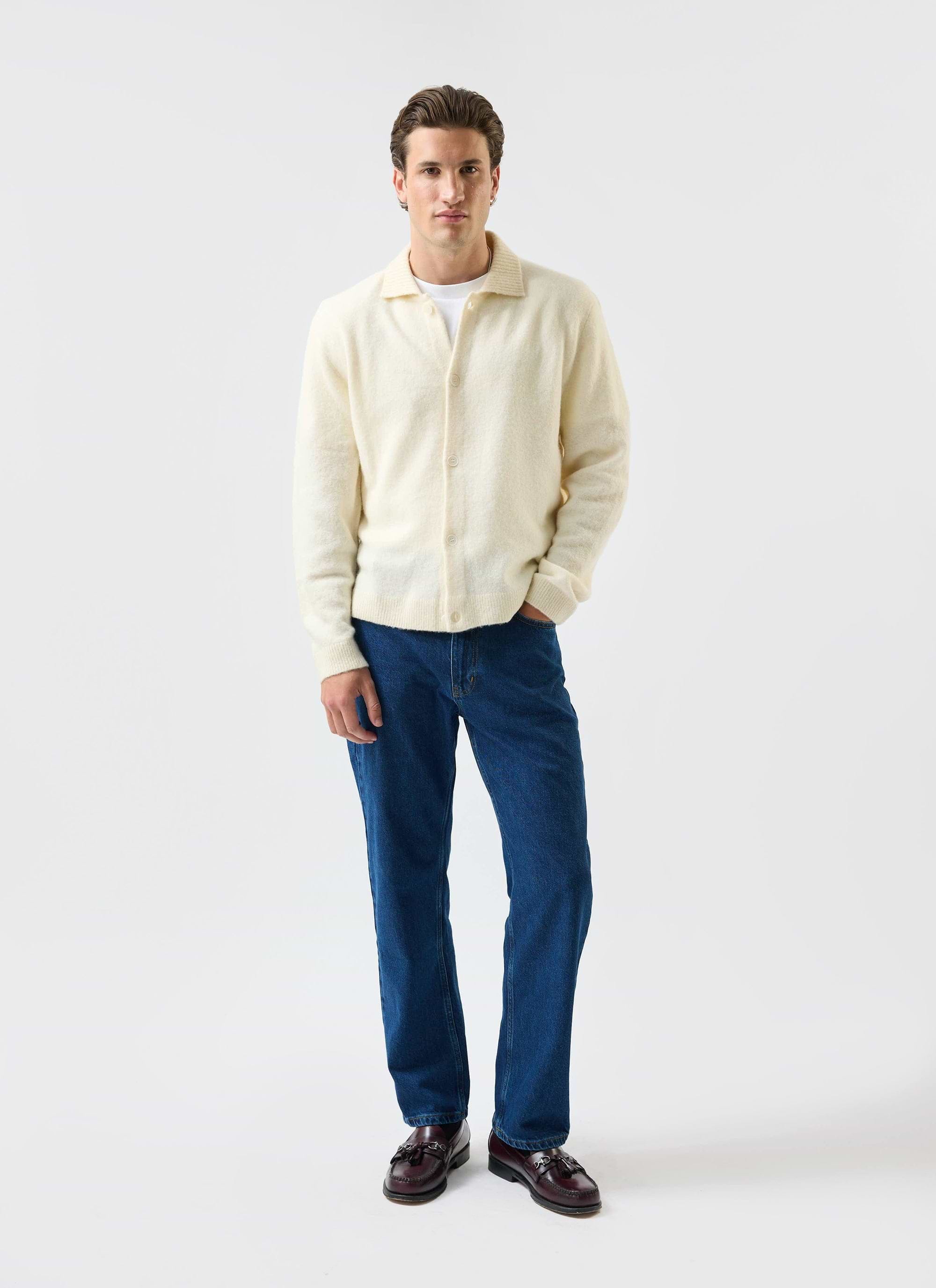 A man models the Percival Archive Wool Knitted Collared Cardigan in ecru cream with blue jeans and loafers.