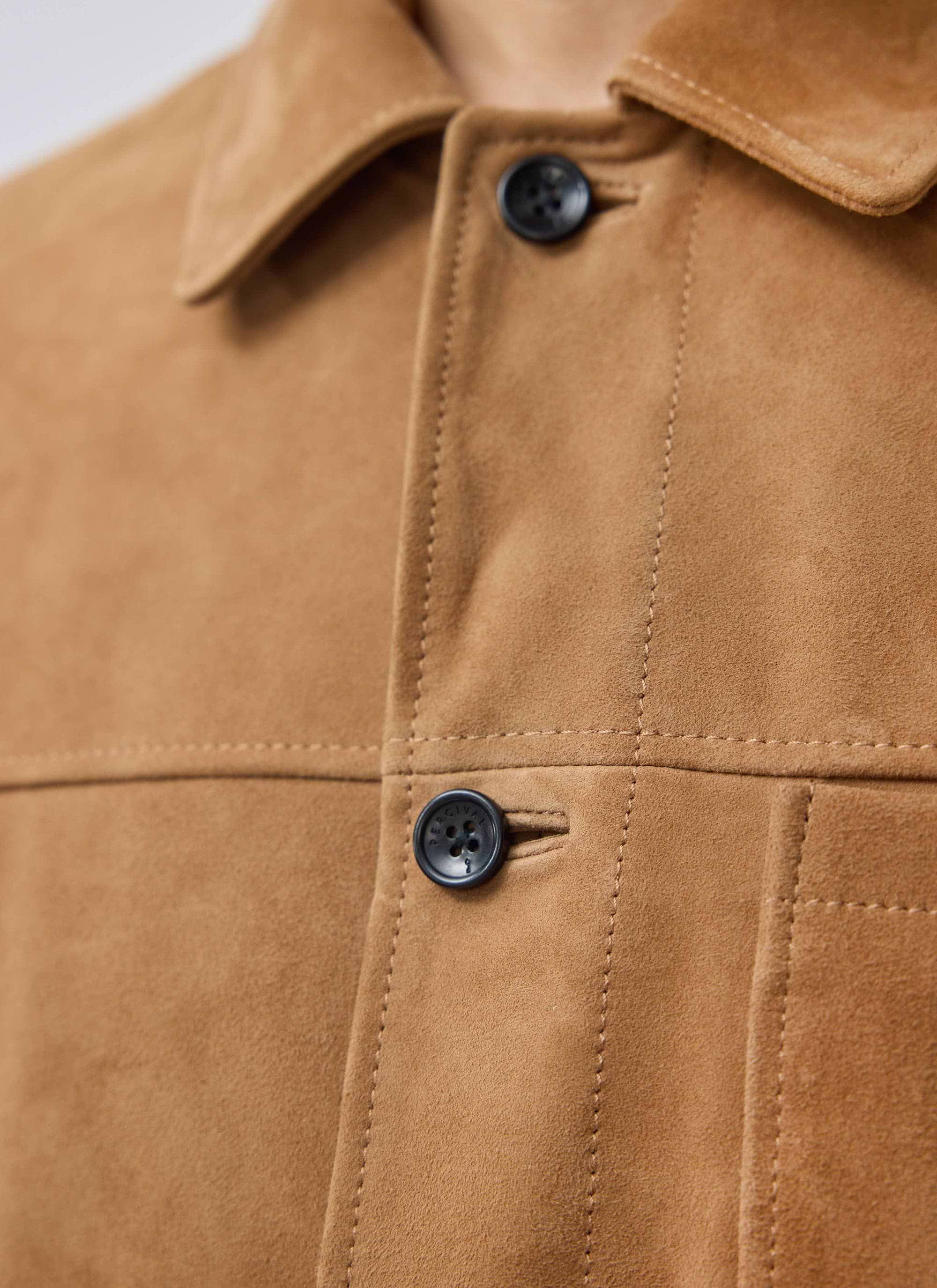 A close-up of the Percival Afterward Suede Chore Jacket in tan, highlighting its soft texture and custom branded buttons.