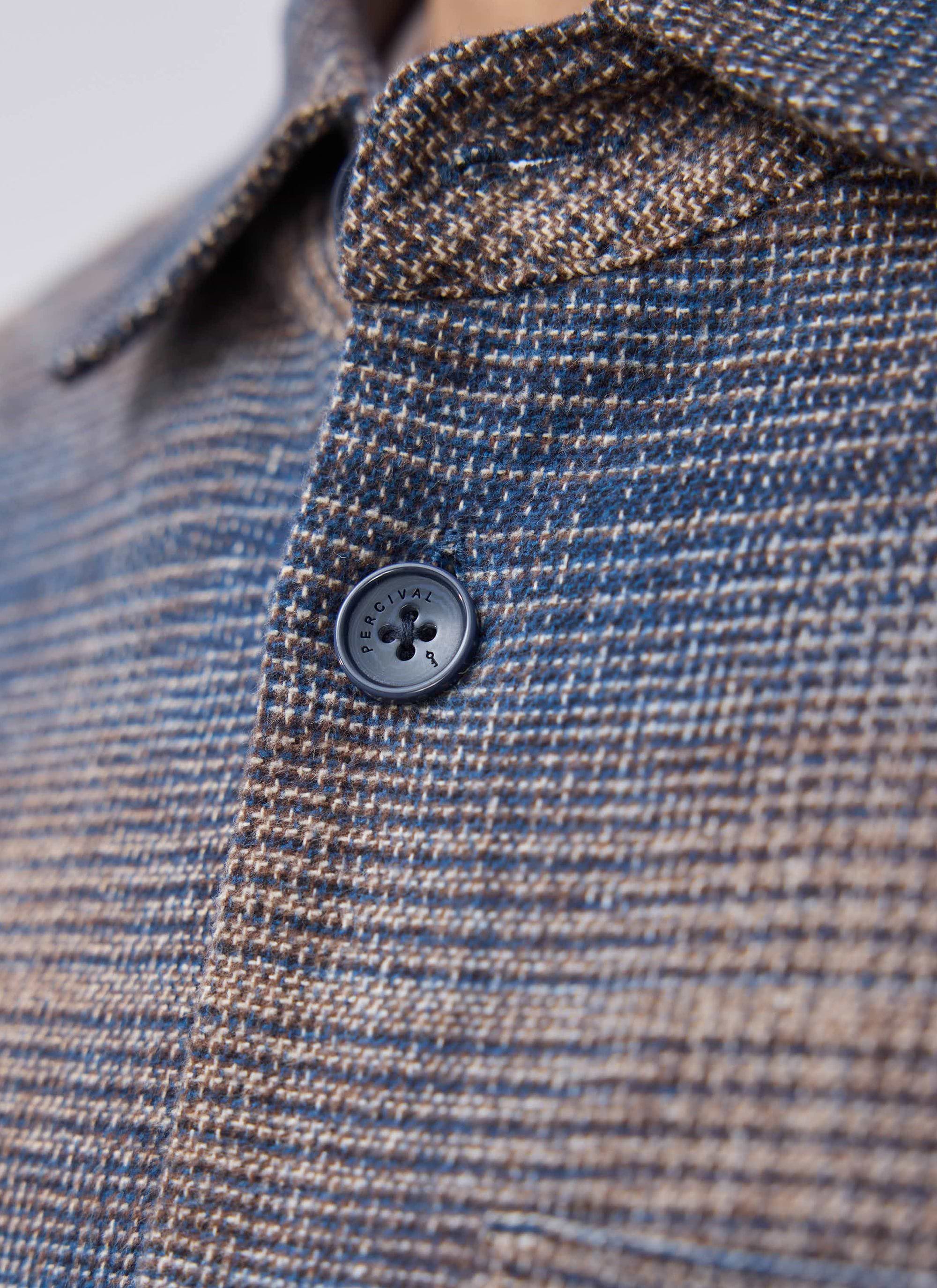 A close-up of the custom branded button on the Percival Luton Check Overshirt in a brown and blue brushed cotton.