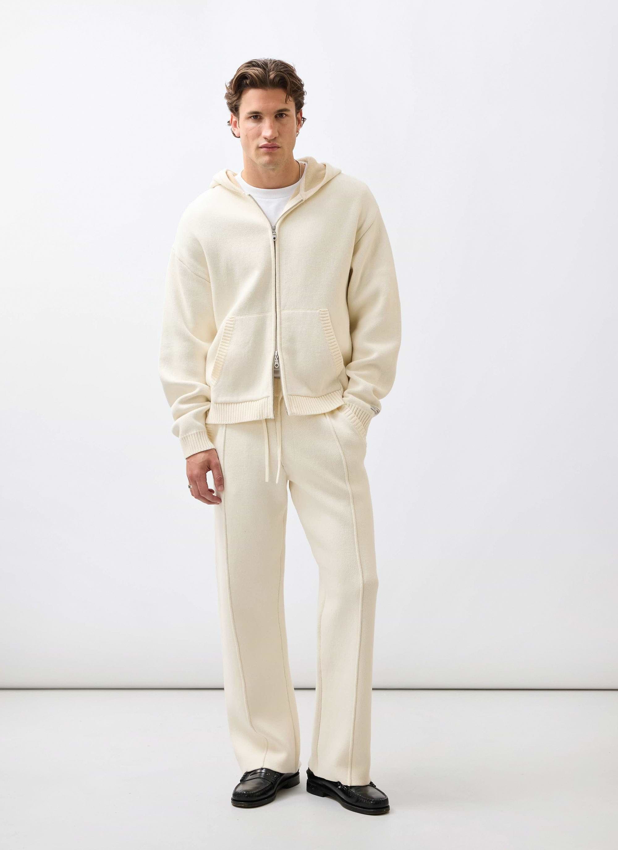 A model wears the Percival Chronicle co-ord set, featuring the ecru knitted straight-leg trackpants and matching zip hoodie.