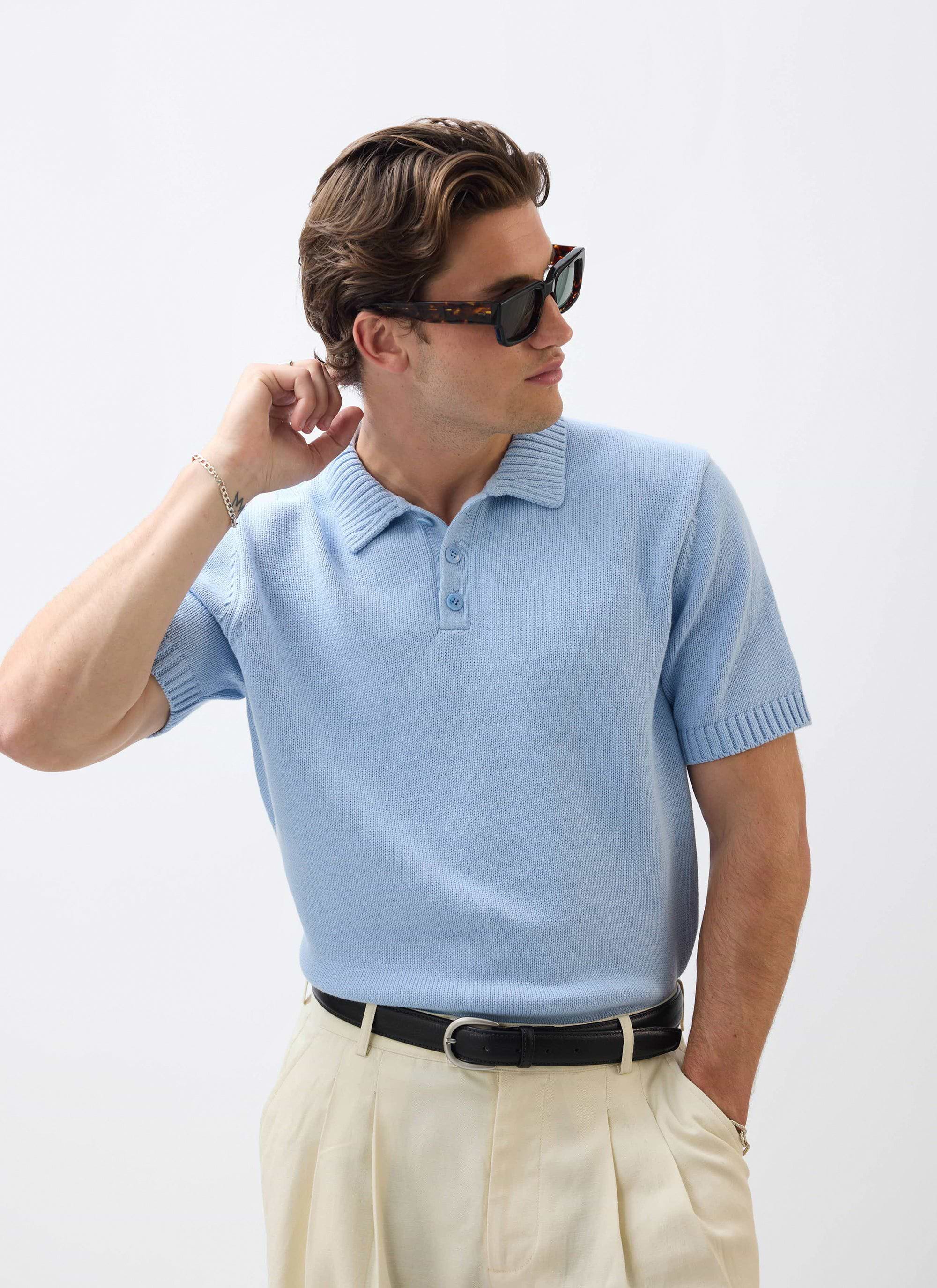A model wears the Percival Verso Short Sleeve Knitted Shirt in heather blue with cream trousers and sunglasses.