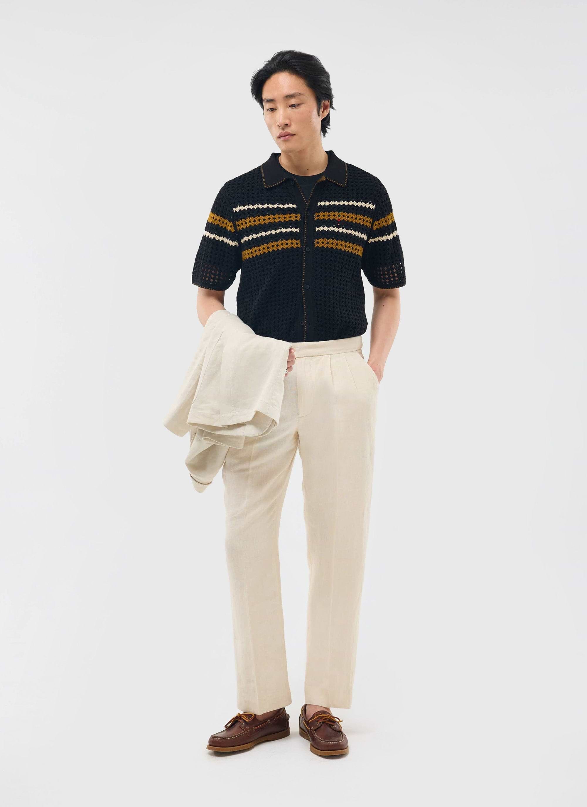 A model wears the black Percival Pesaro Knitted Shirt, featuring mustard and white stripes, with cream trousers.