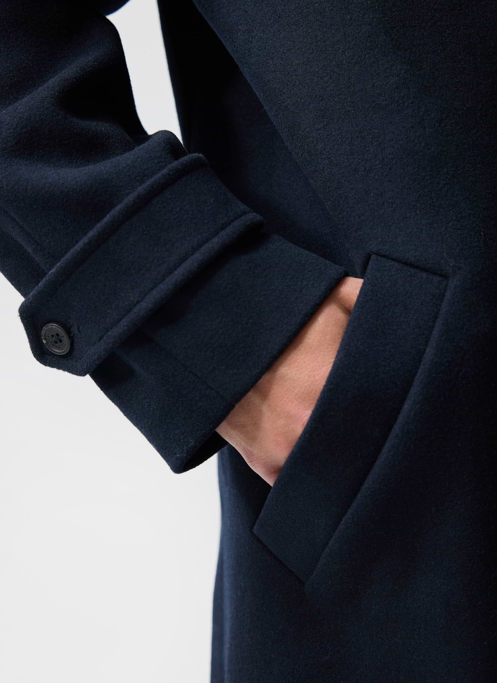 Close-up of the Percival Men's Wool Car Coat in navy, showing the cuff detail with branded button and side pocket.