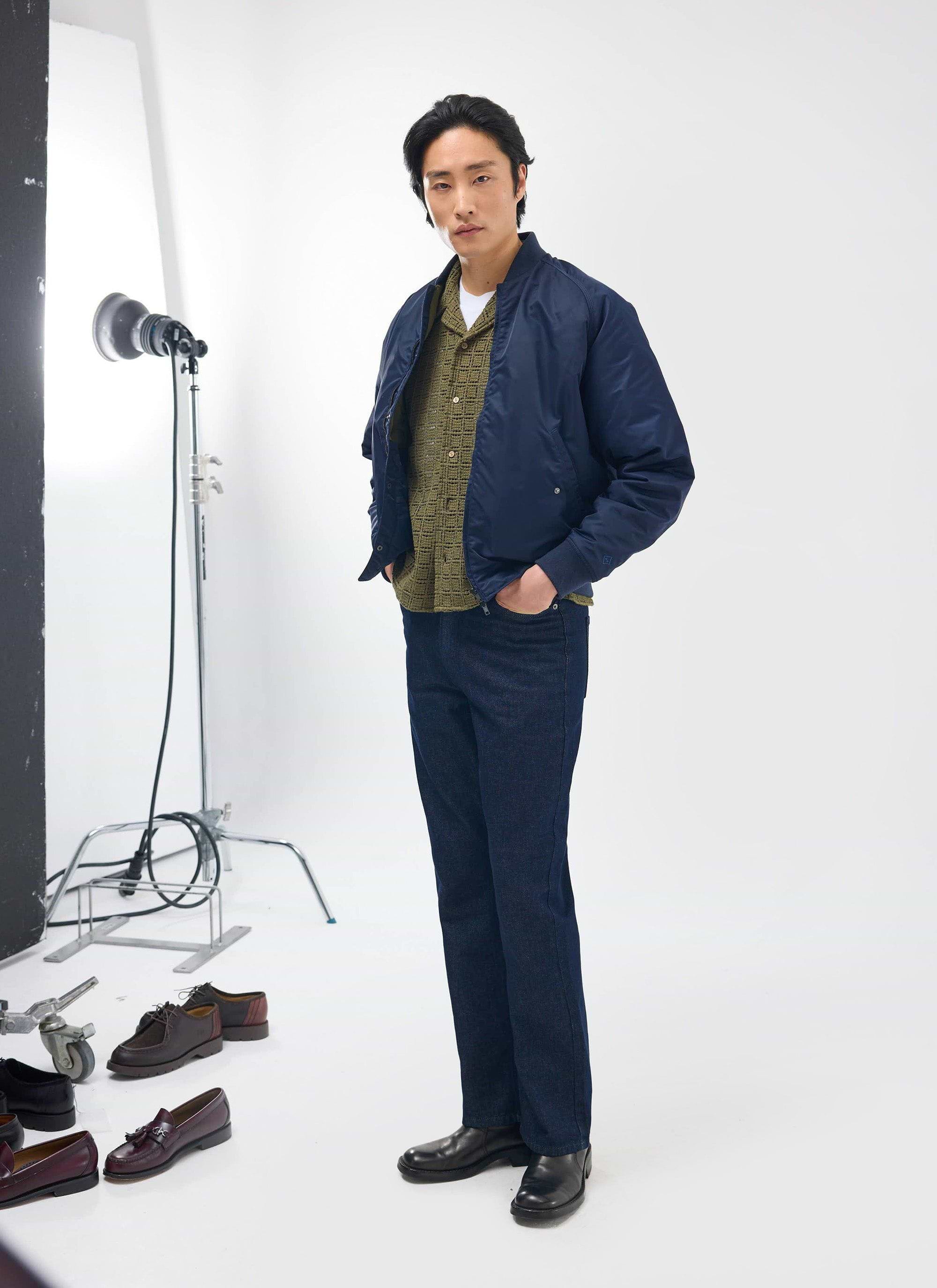 A male model wears the Percival Palermo Crochet Cuban Shirt in olive green, styled under a navy bomber jacket in a studio.