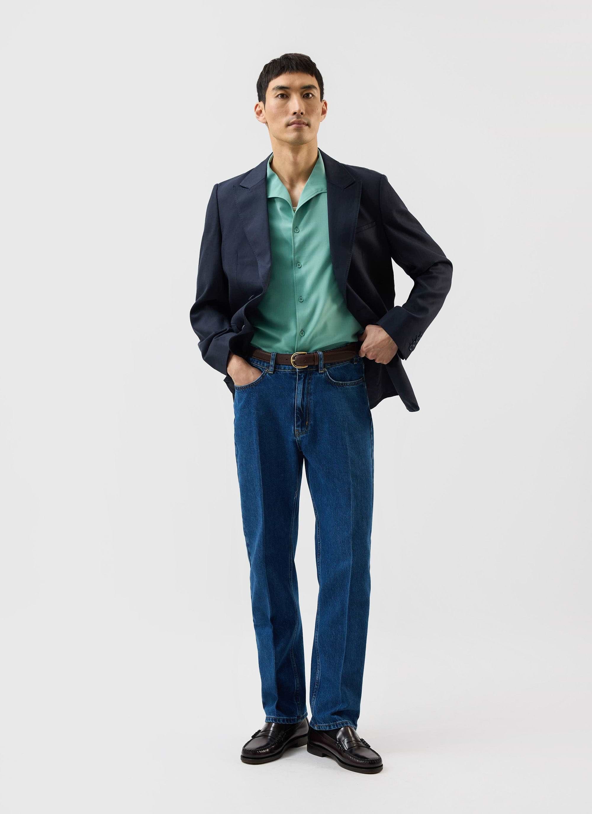 A man models the Percival x Warren Drape Cuban Shirt in mint green, styled with a dark blazer and blue jeans.
