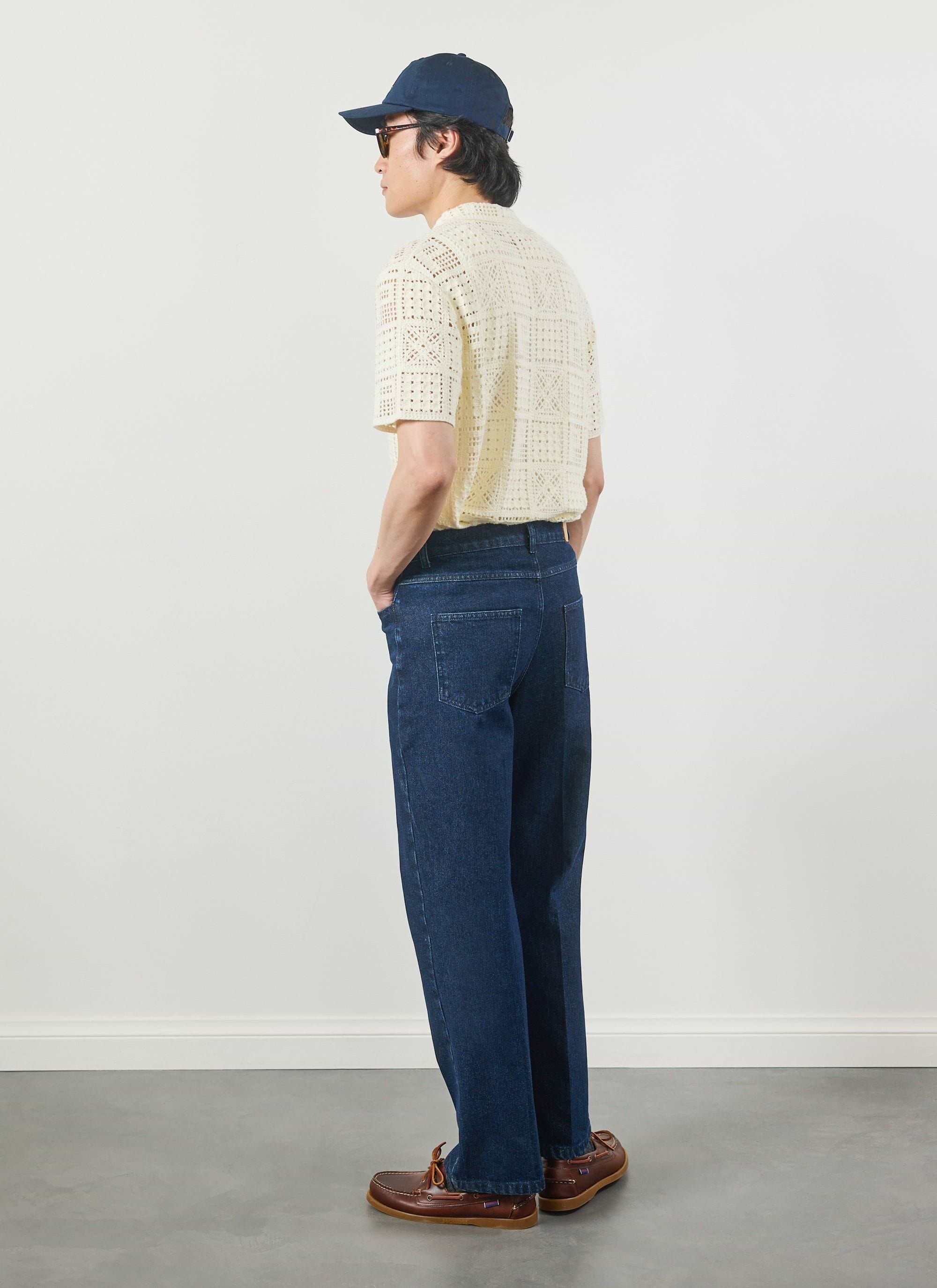 A model wearing the Percival Crochet Groundsman Shirt in ecru, styled with dark denim jeans and a cap, seen from behind.