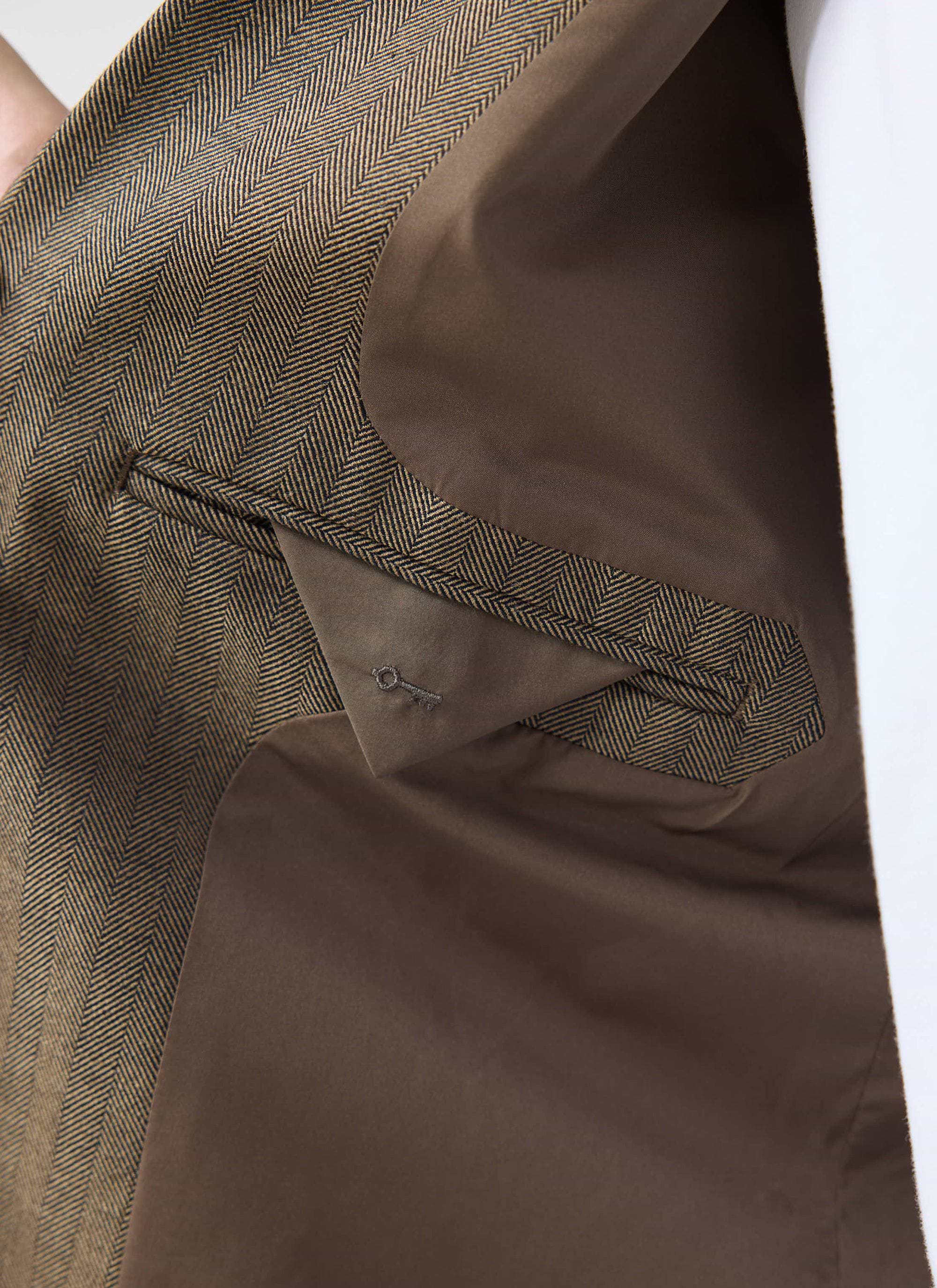 A close-up of the Percival Grounds Blazer showing the oak herringbone fabric, brown lining and pocket with key embroidery.