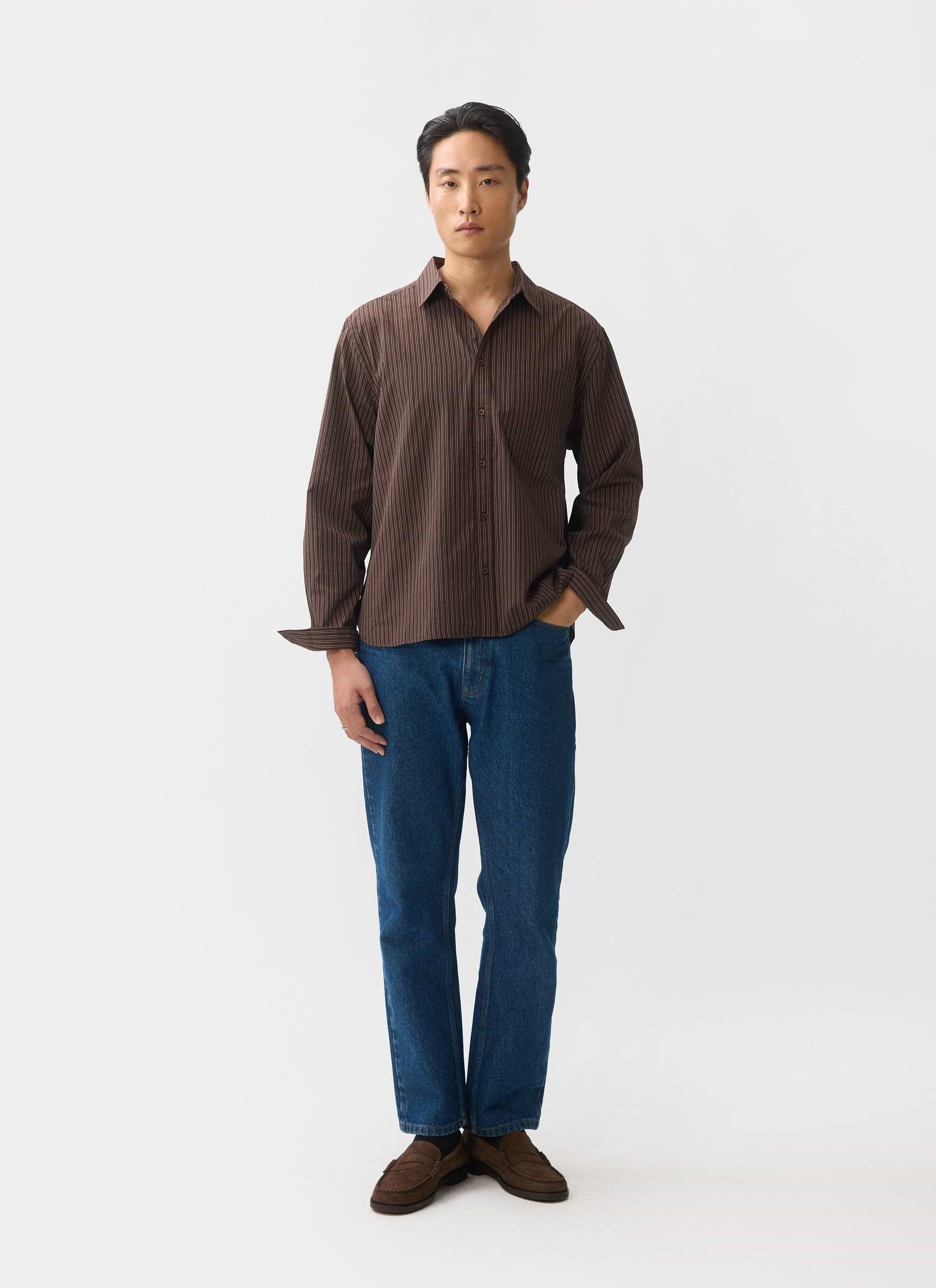 A model wears the Percival Clancy Striped Long Sleeve Shirt in brown, paired with blue jeans against a white background.