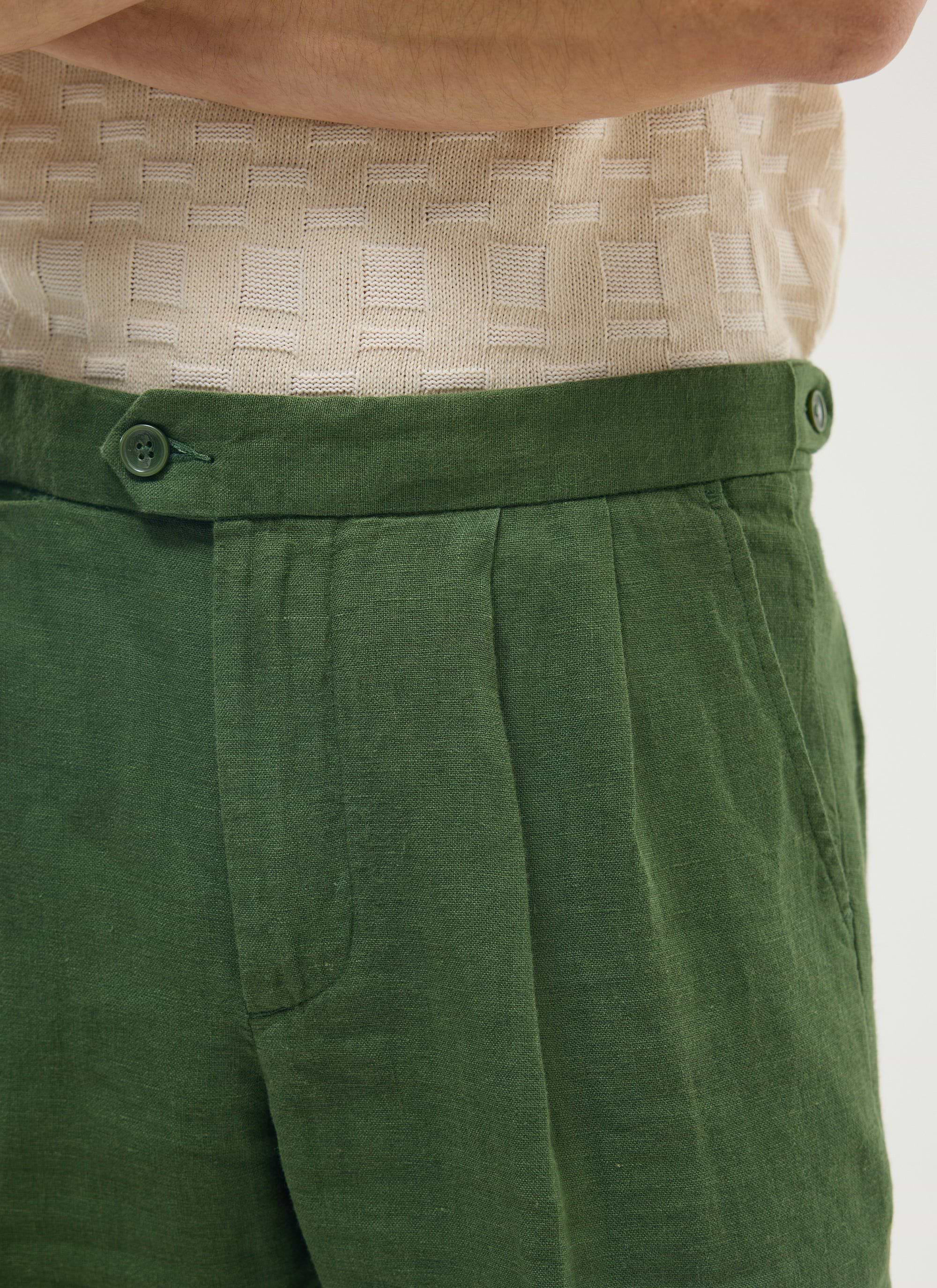 Close up of the waistband and pleat on the Percival forest green linen tailored trousers, worn with a cream knit top.