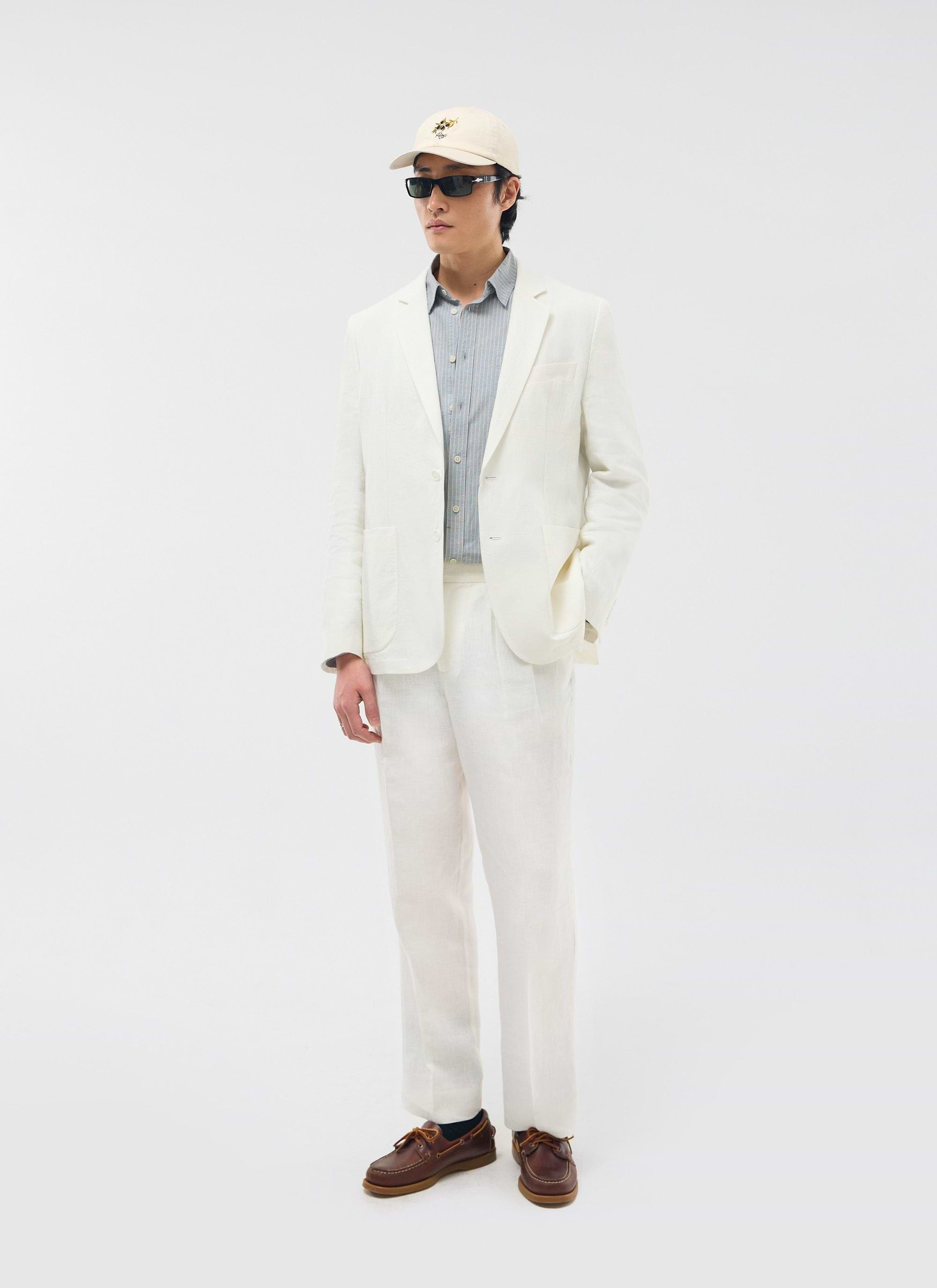 A model wears the white Percival Relaxed Tailored Linen Blazer with matching trousers, a striped shirt, and sunglasses.