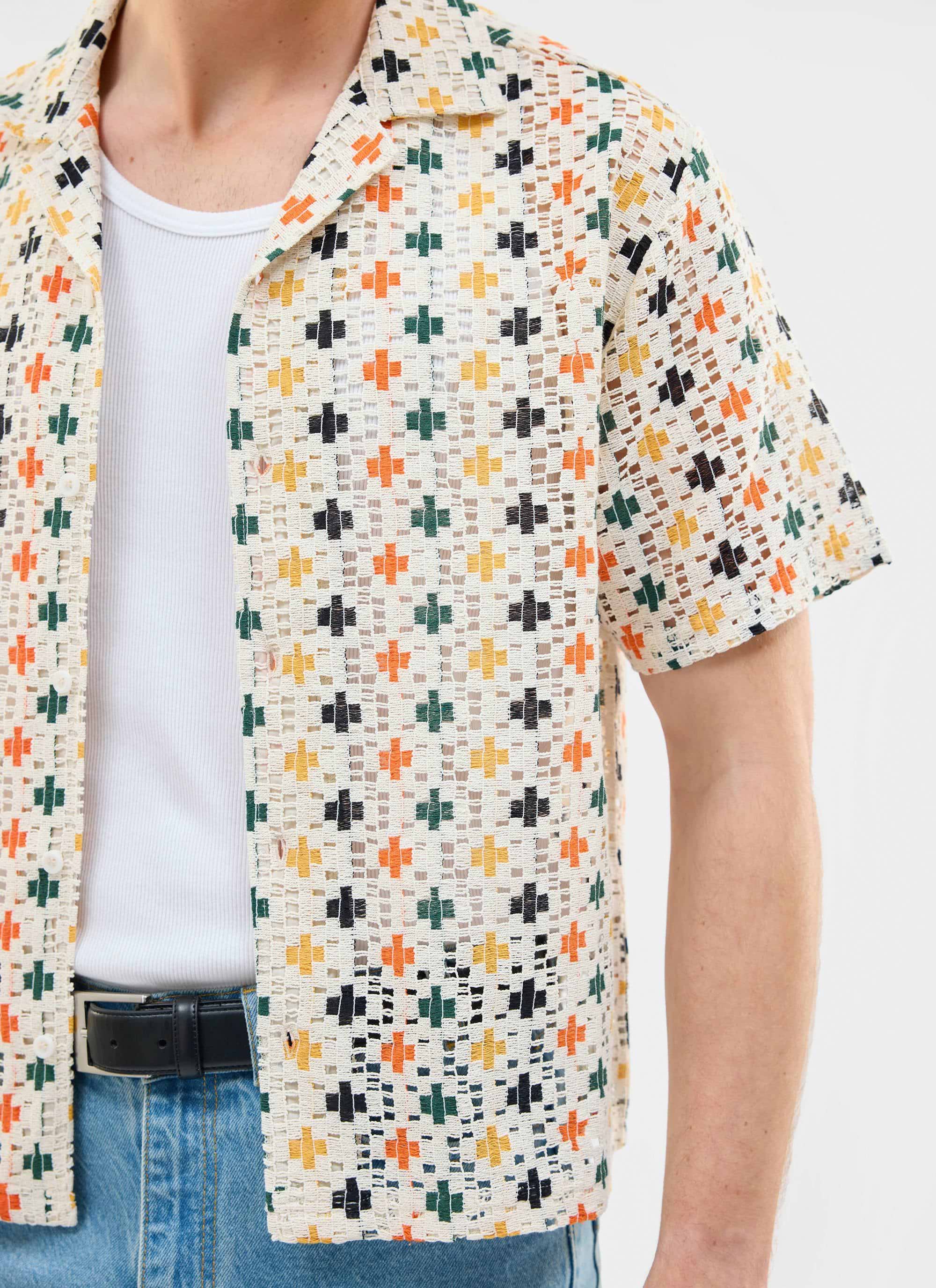 A close-up shot of a man wearing the Percival Bailing Crochet Cuban Shirt, open over a white vest with blue jeans.