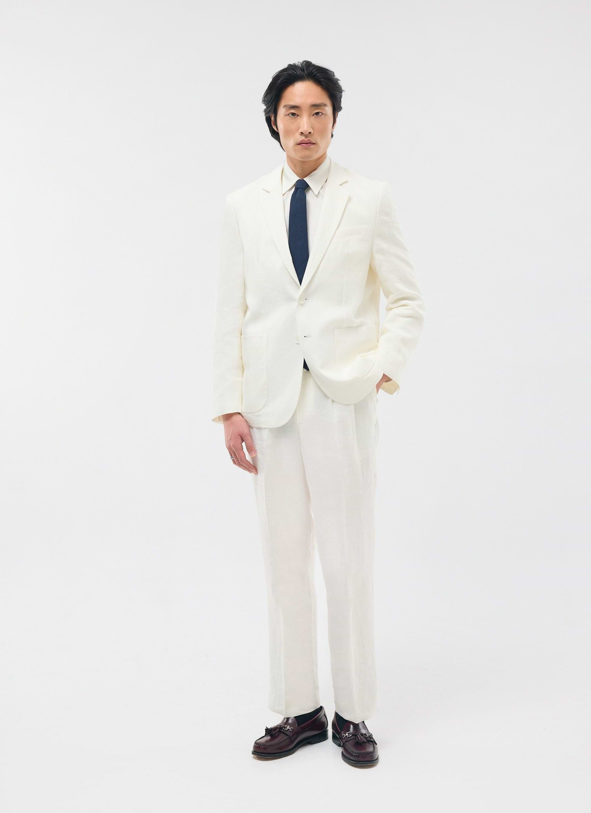 A model wears the full Percival Relaxed Tailored Linen Suit in white, styled with a navy tie and brown loafers.