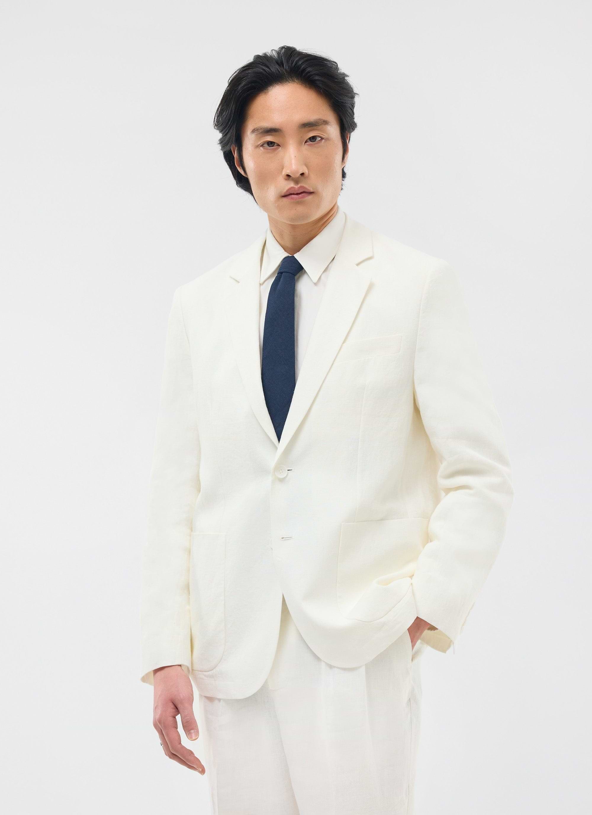 A model wears the Percival Relaxed Tailored Linen Blazer in white, styled with a white shirt and navy tie.