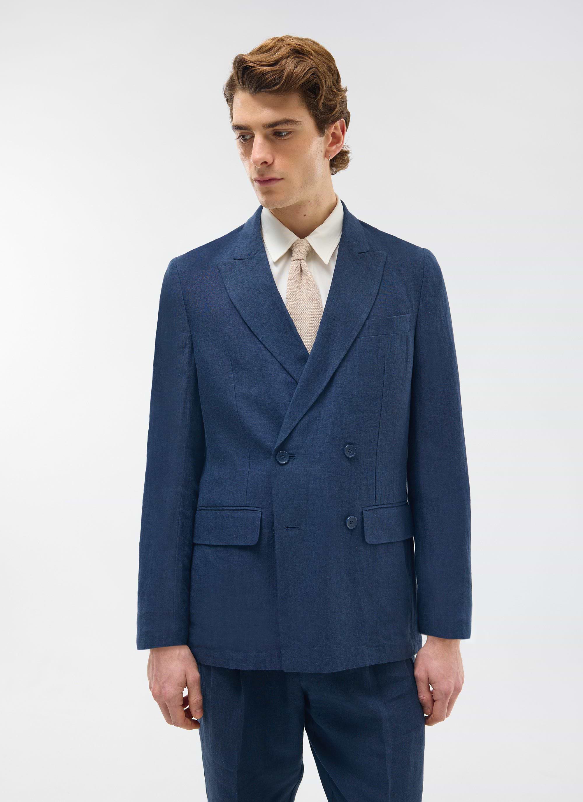 A model wears the full Percival navy linen suit, featuring the double-breasted blazer, with a white shirt and cream tie.