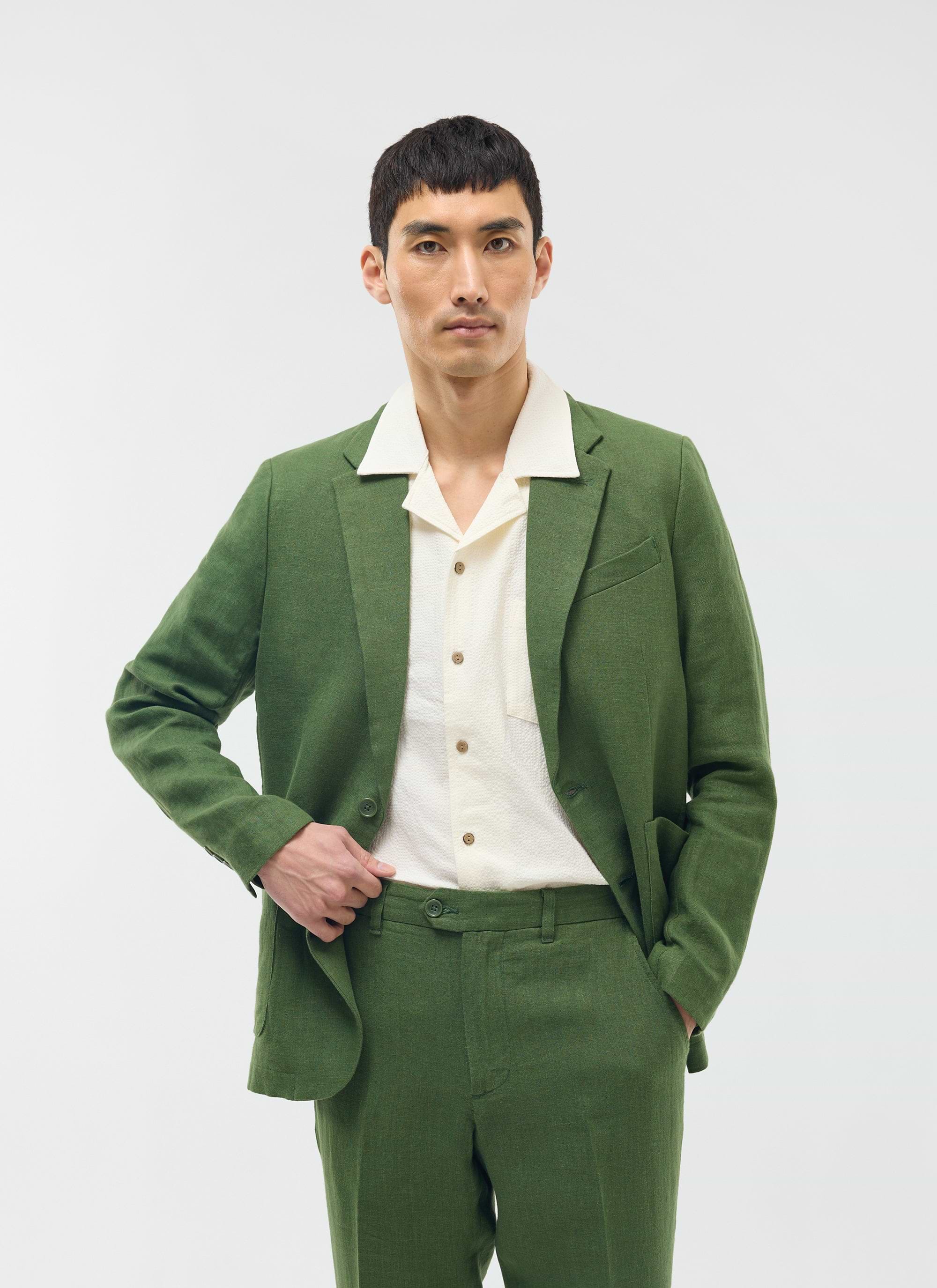 A model wears the Percival forest green linen blazer and matching trousers over a cream short-sleeved shirt.