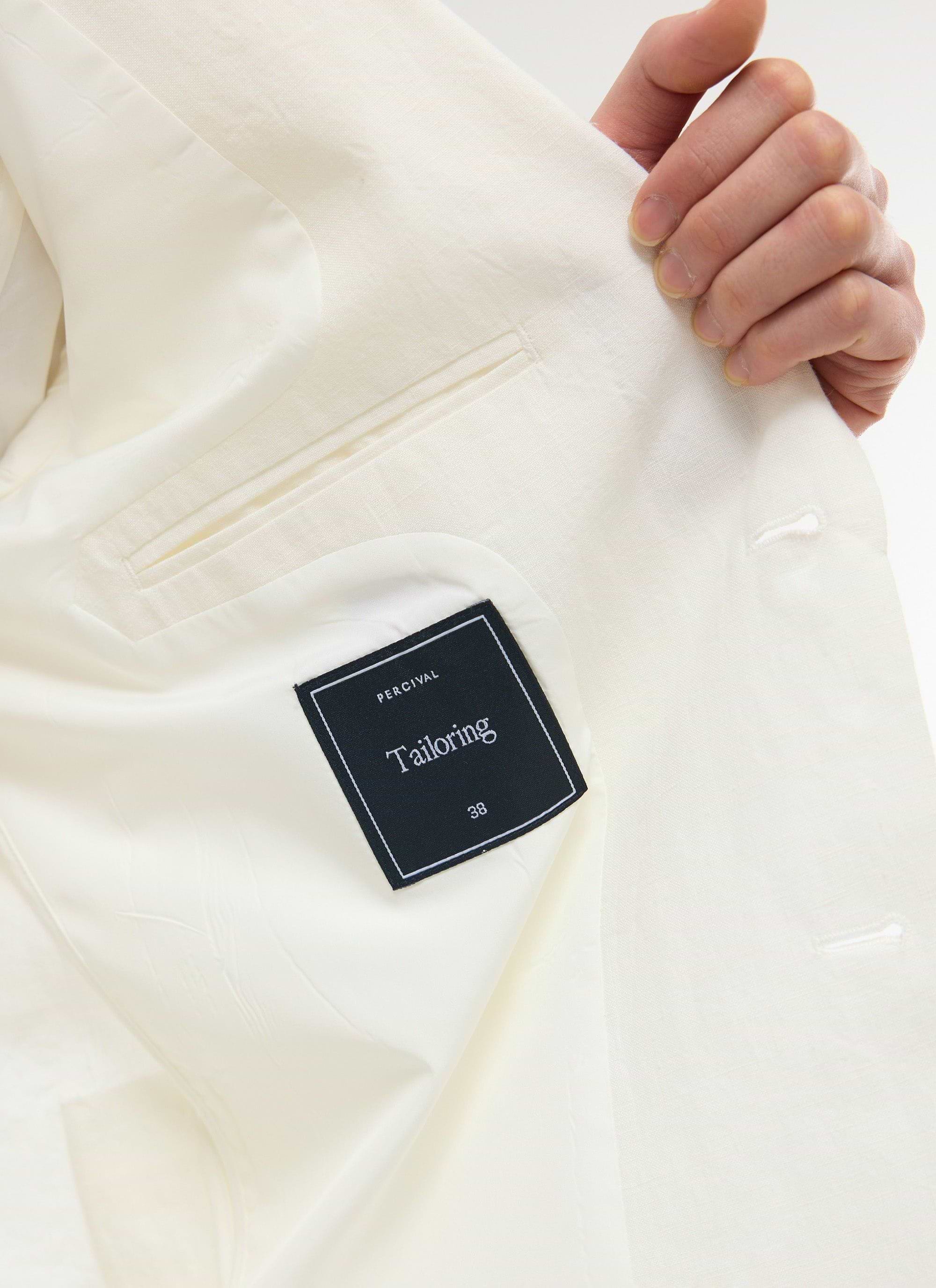 A close-up of the white Relaxed Tailored Linen Blazer, showing the inner Percival tailoring label and pocket detail.
