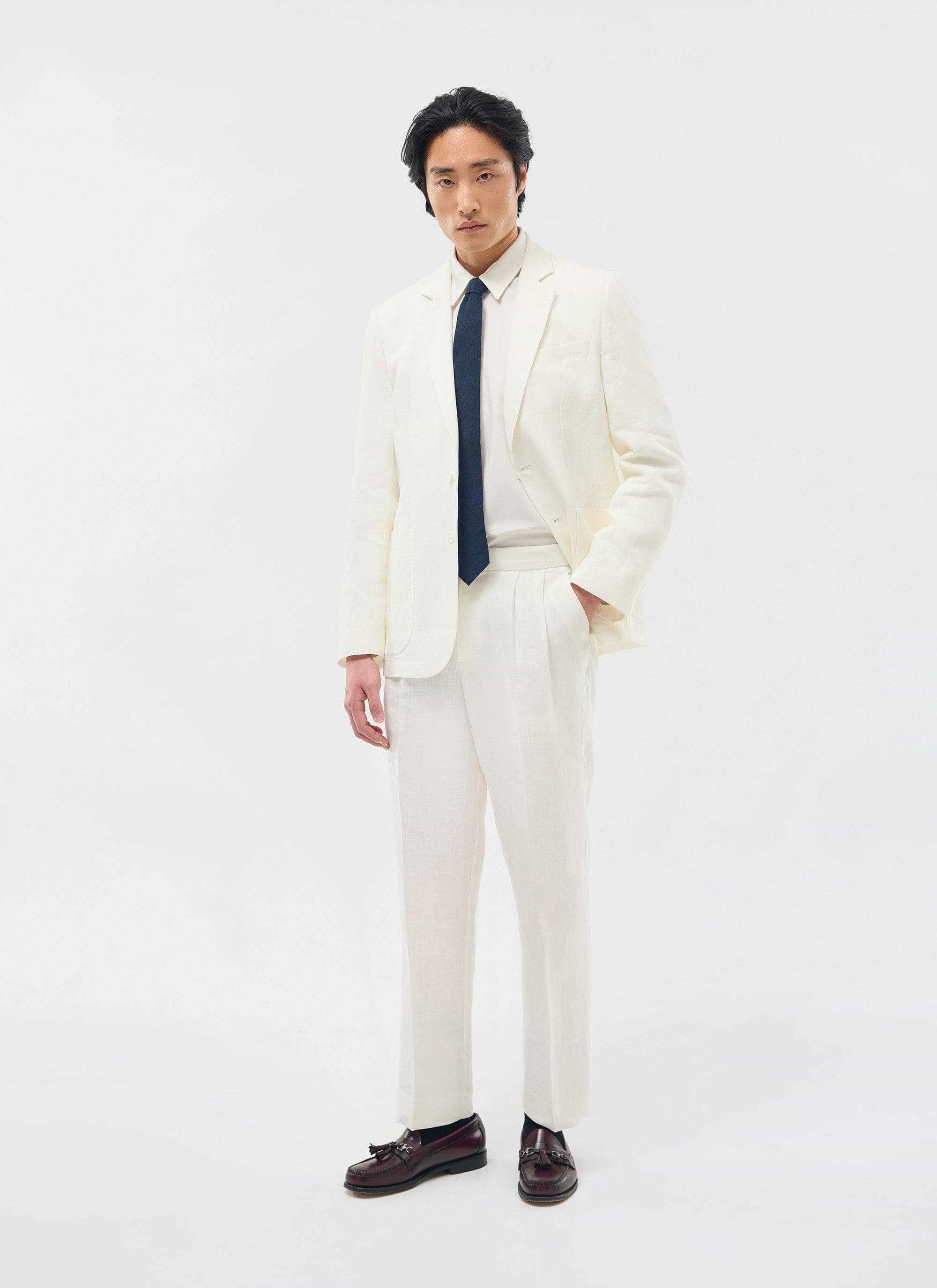 Model wears the Percival Relaxed Tailored Linen Blazer in white with matching trousers, a navy tie, and burgundy loafers.