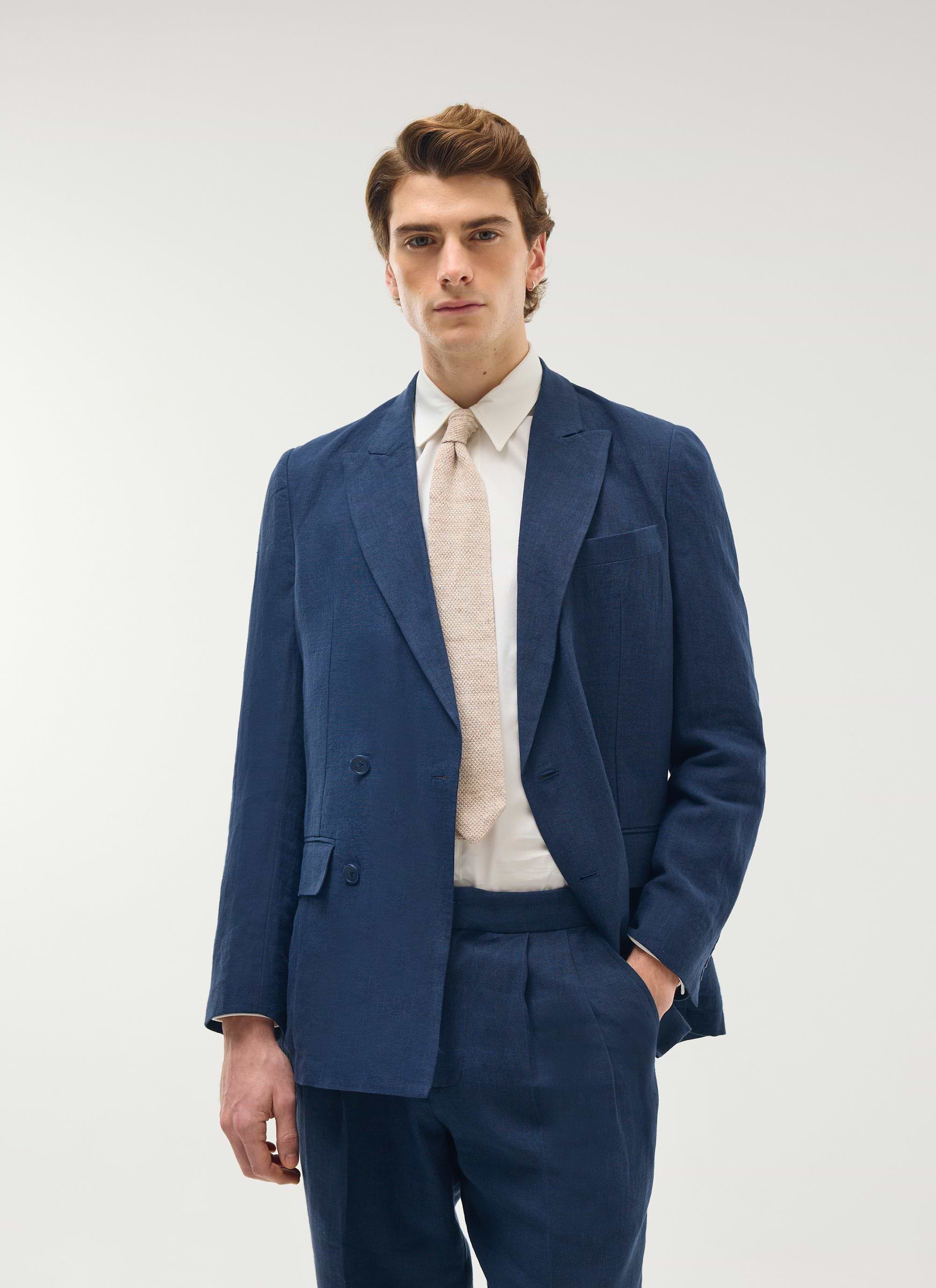 Model wears the Percival navy linen double-breasted blazer and matching trousers with a white shirt and light tie.