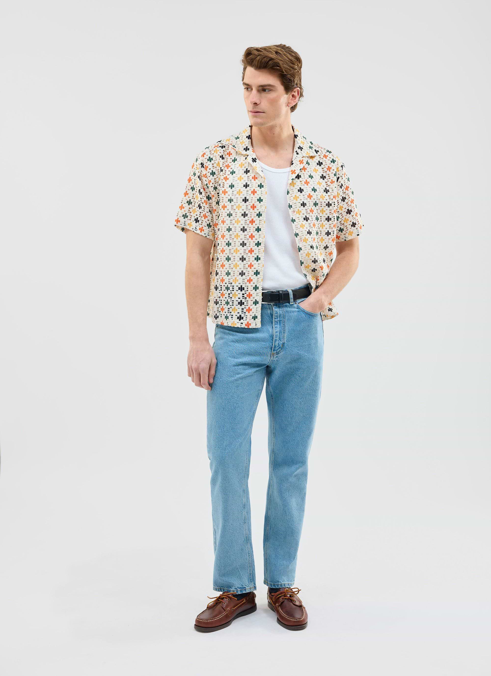 A man models the Percival Bailing Crochet Cuban Shirt with a white vest and blue jeans against a white studio background.