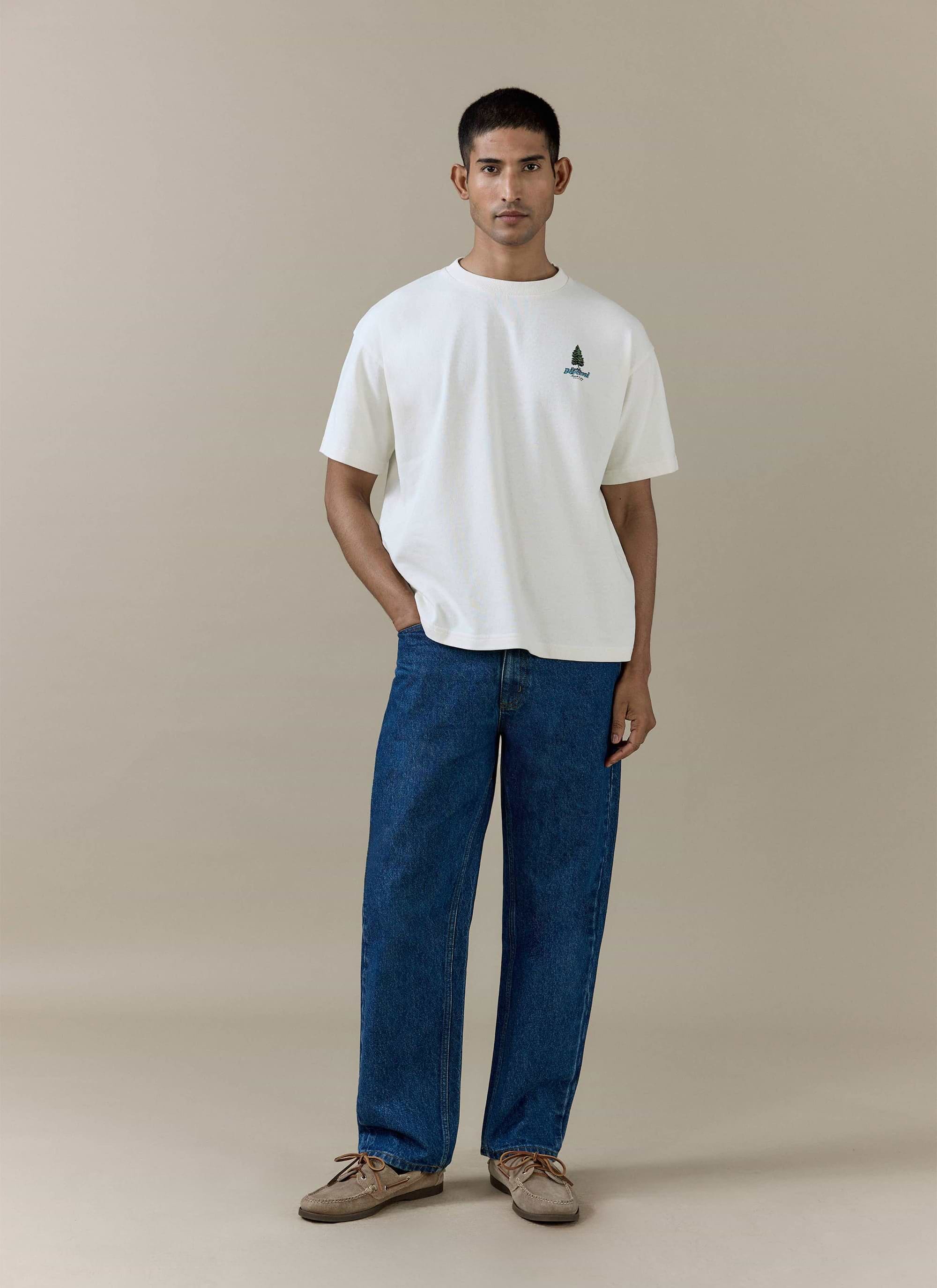 Percival Arnold Oversized T Shirt in cream organic cotton with a pine tree chest graphic, worn with dark blue jeans.