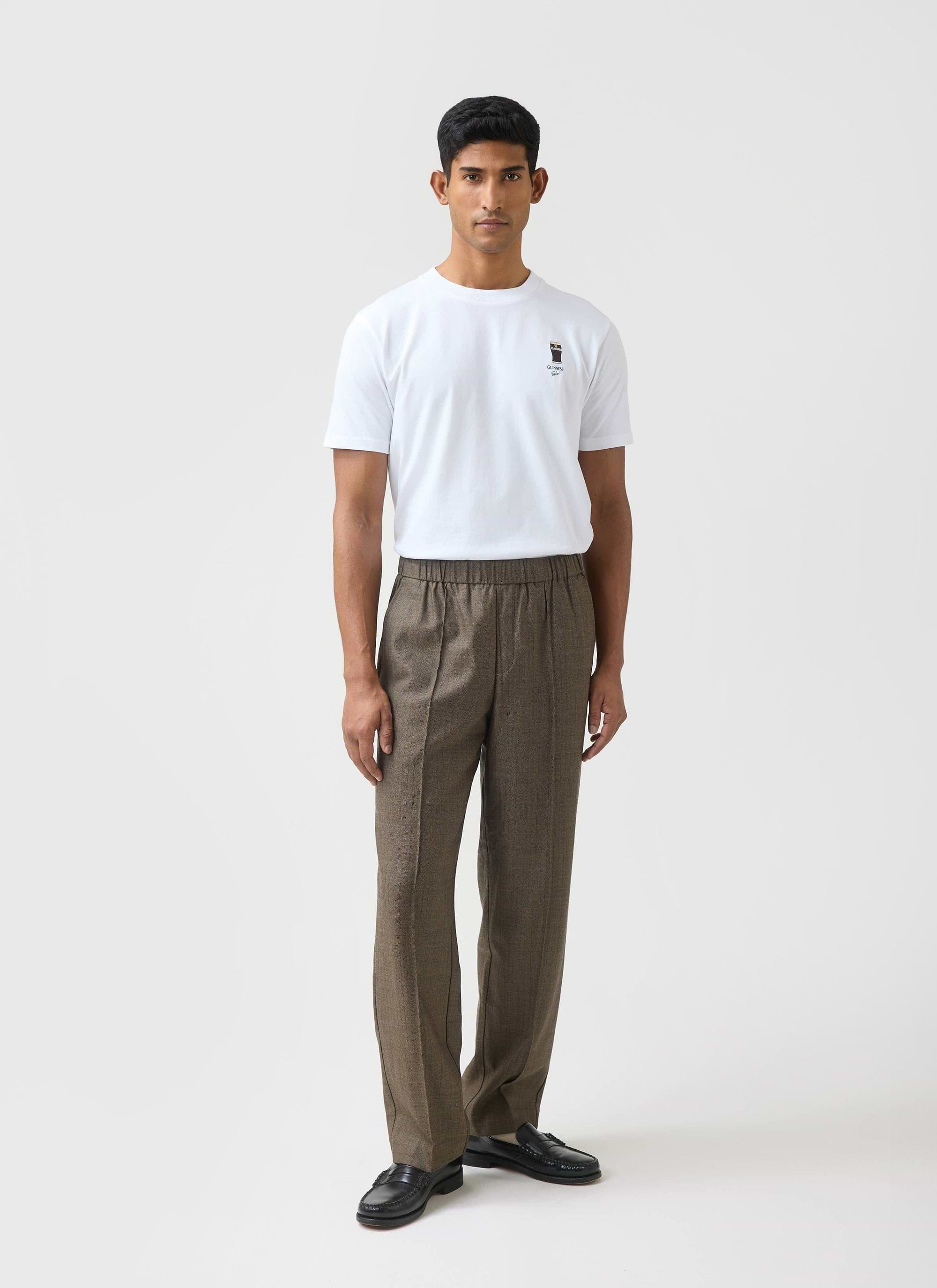 A model wears the white Percival x Guinness Stout T Shirt with brown checked trousers against a white background.