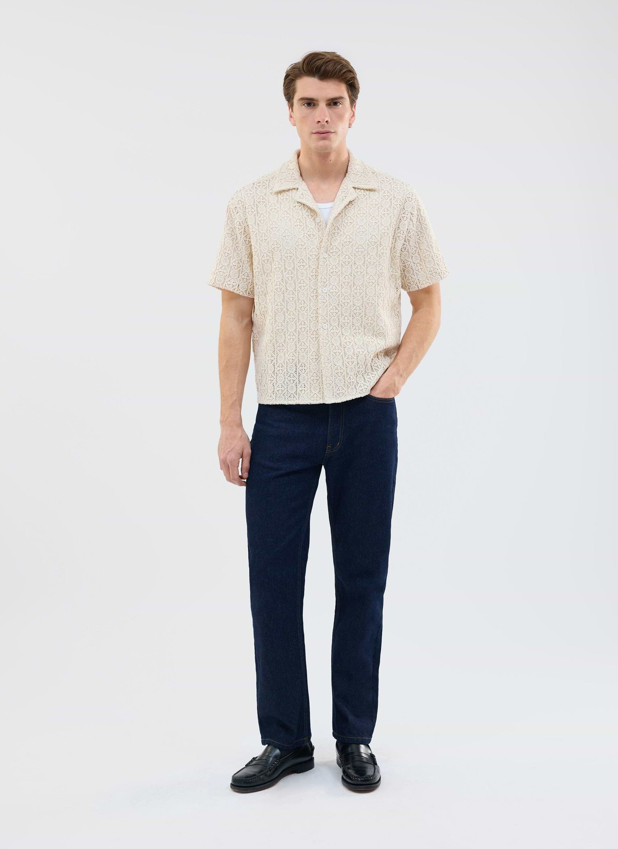 A model wears the Percival Elio Crochet Cuban Shirt in ecru, styled with dark denim jeans and black loafers.