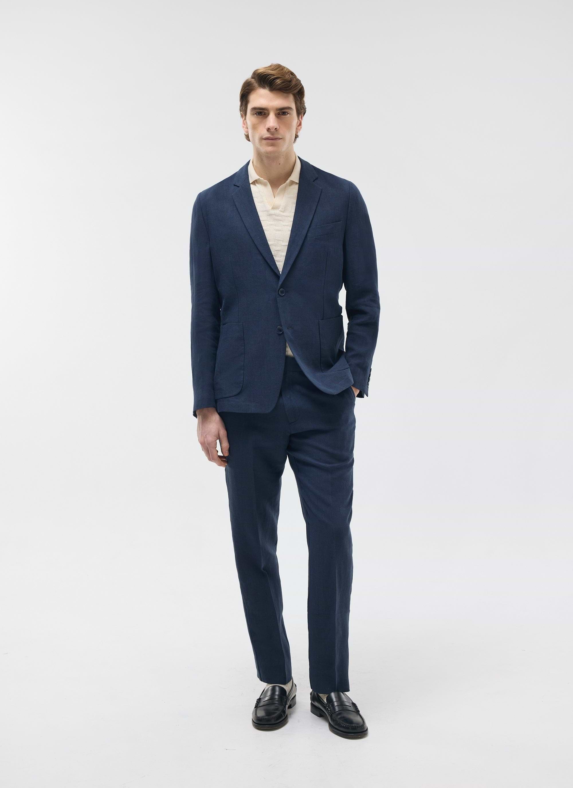 A model wears the Percival Tailored Linen Trousers in navy, styled with the matching blazer and a cream polo shirt.
