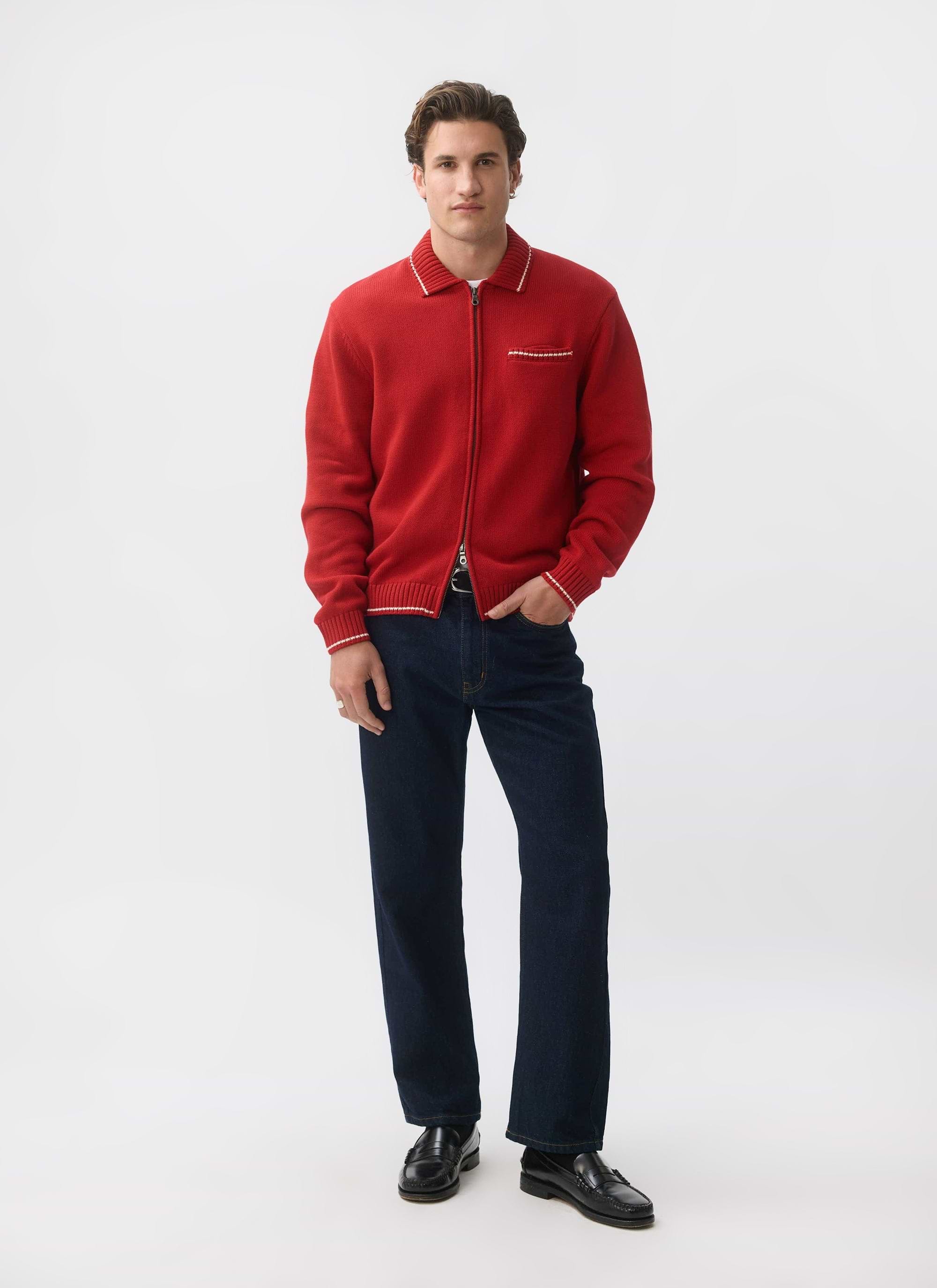 A man models the red Gardner Dense Knitted Zip Cardigan from Percival, styled with dark jeans and black loafers.