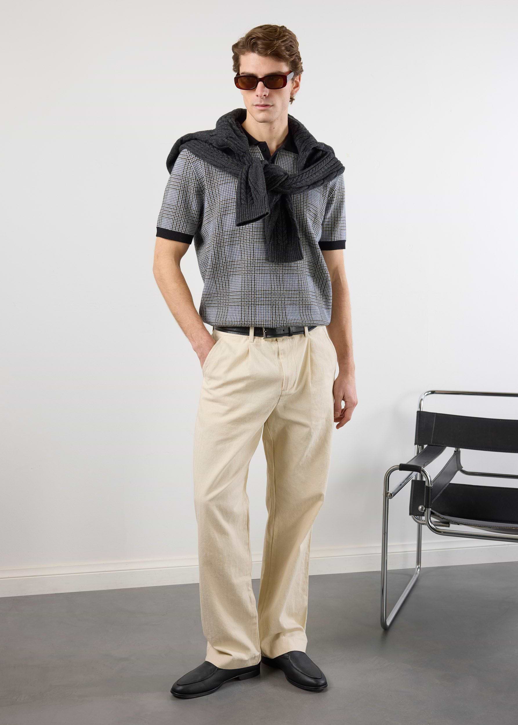 A model wears the Percival Casa Martini Knitted Polo in navy puppytooth, styled with beige trousers and a grey jumper.