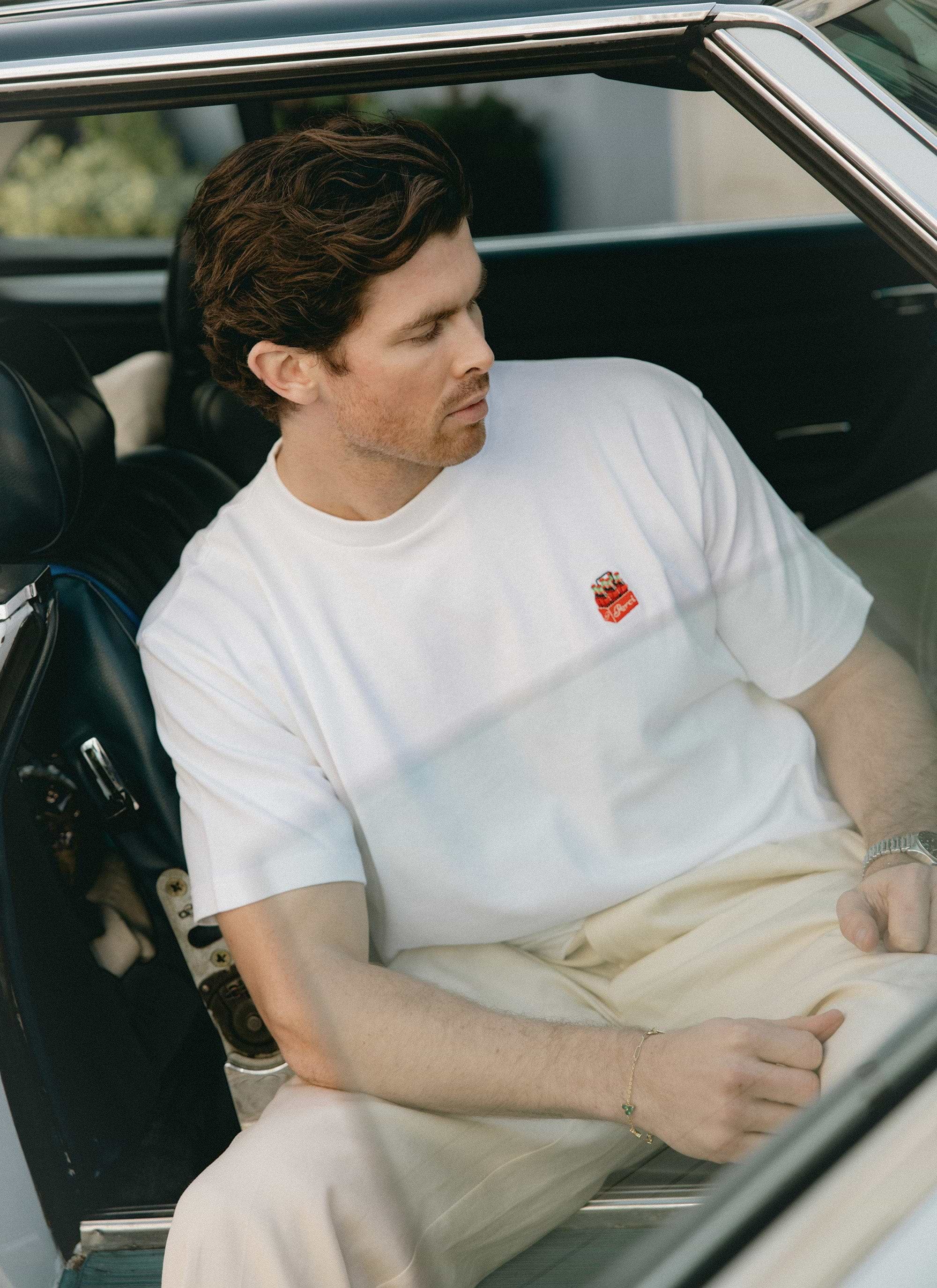 Lifestyle shot of a model wearing the white Percival Soda Bottles Oversized Embroidered T Shirt in a vintage car.