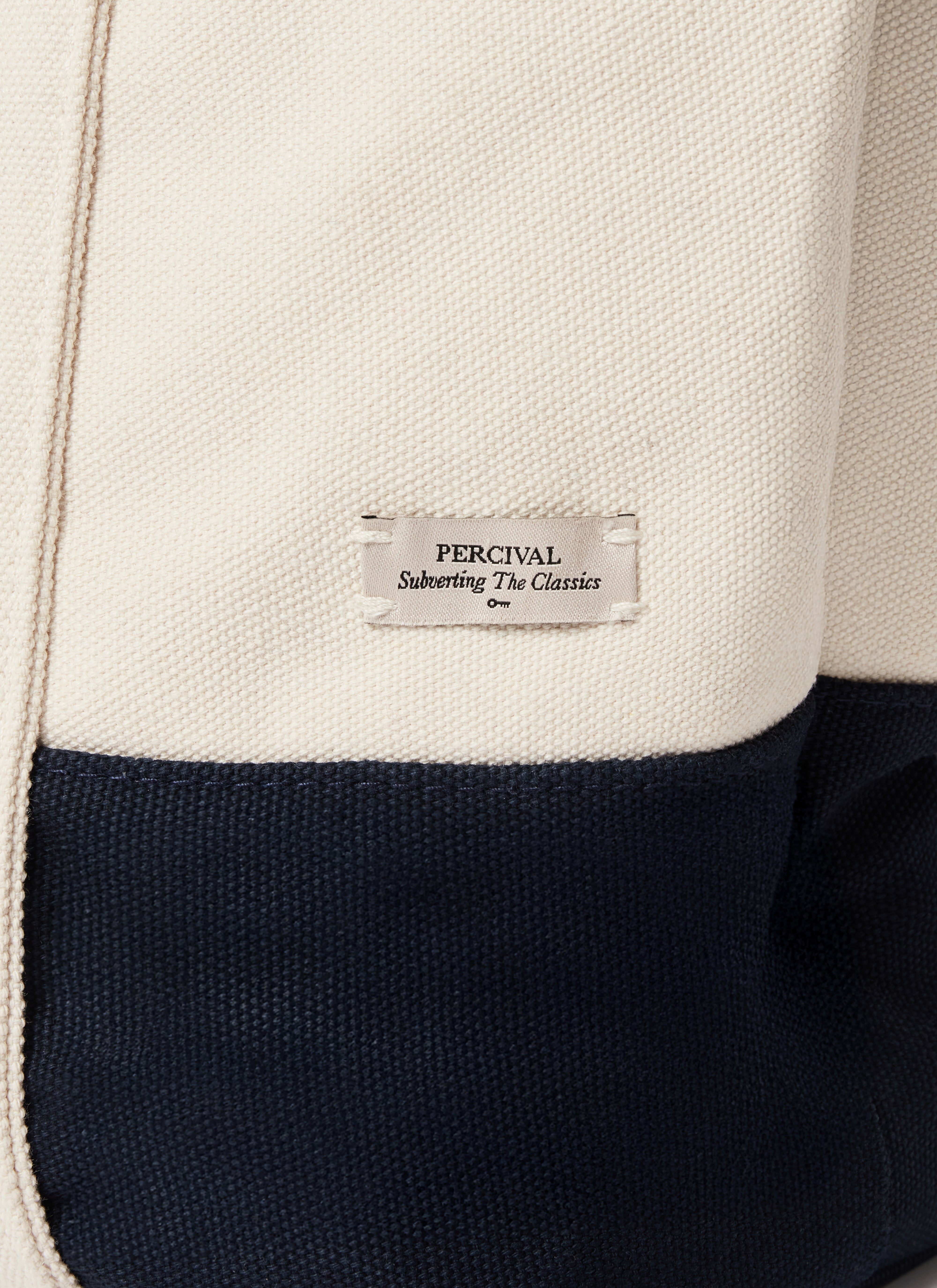 A close-up of the Percival woven label on the navy and cream Brighton & Hove Albion F.C. canvas tote bag.