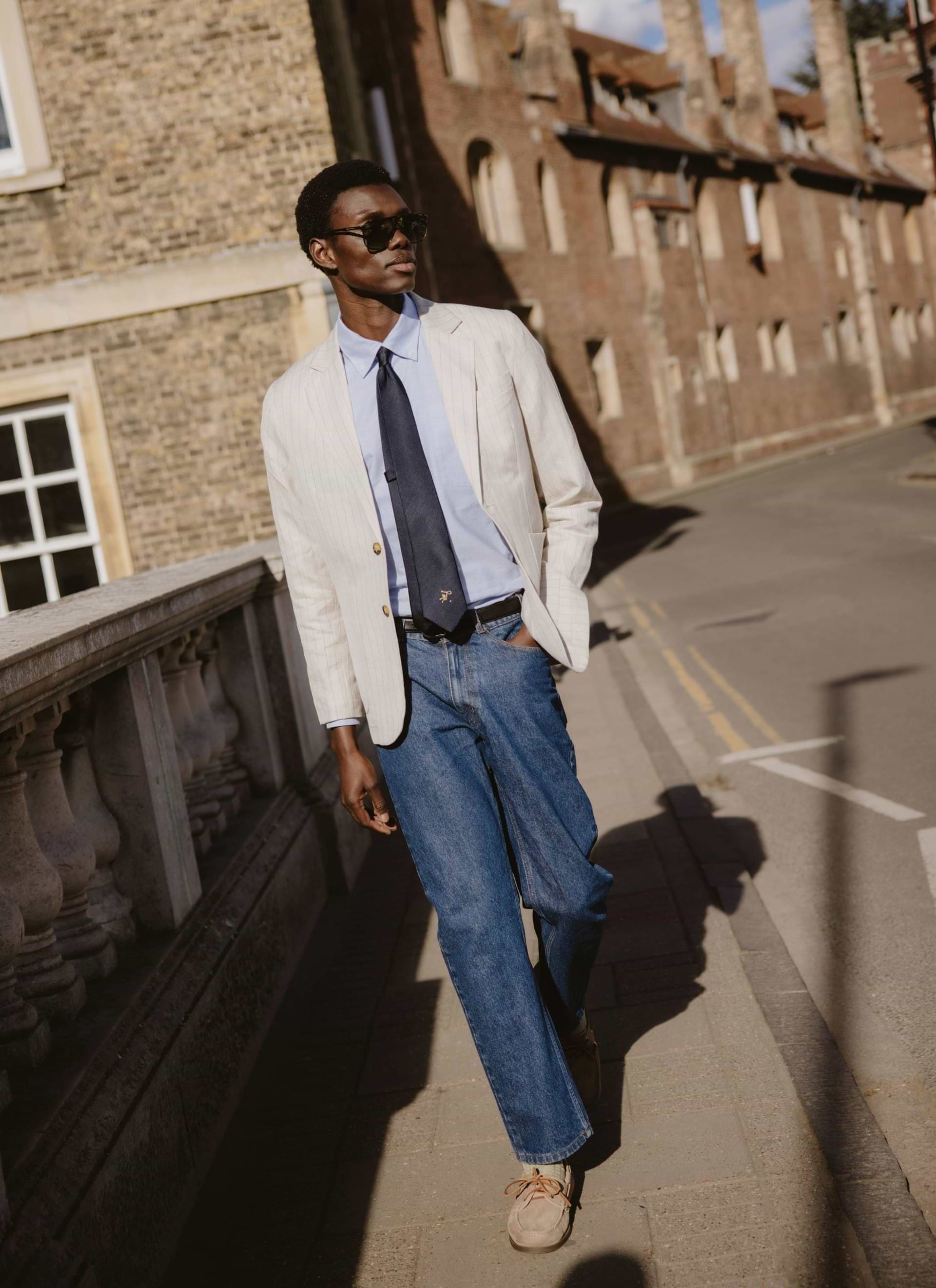 The navy silk World Key Tie from Percival, featuring a gold motif and styled on a model in a pinstripe blazer.
