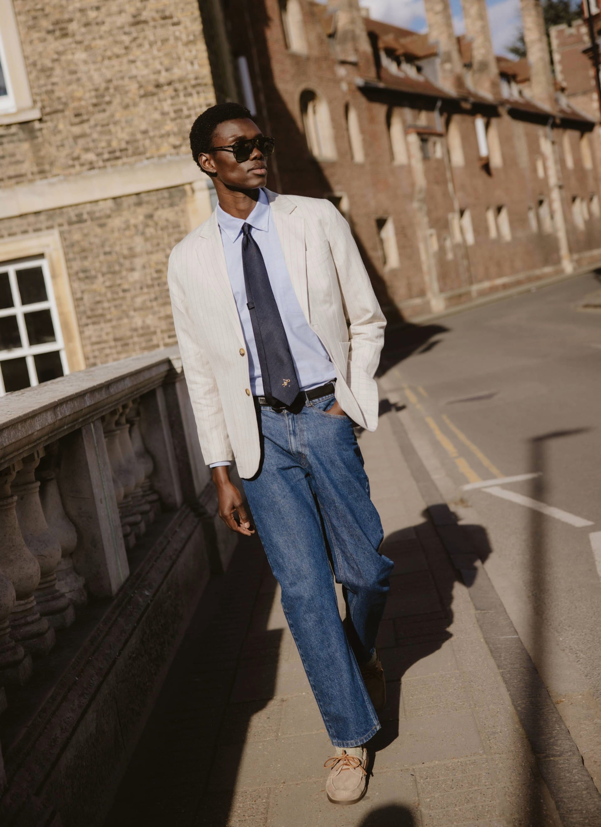 The navy silk World Key Tie from Percival, featuring a gold motif and styled on a model in a pinstripe blazer.