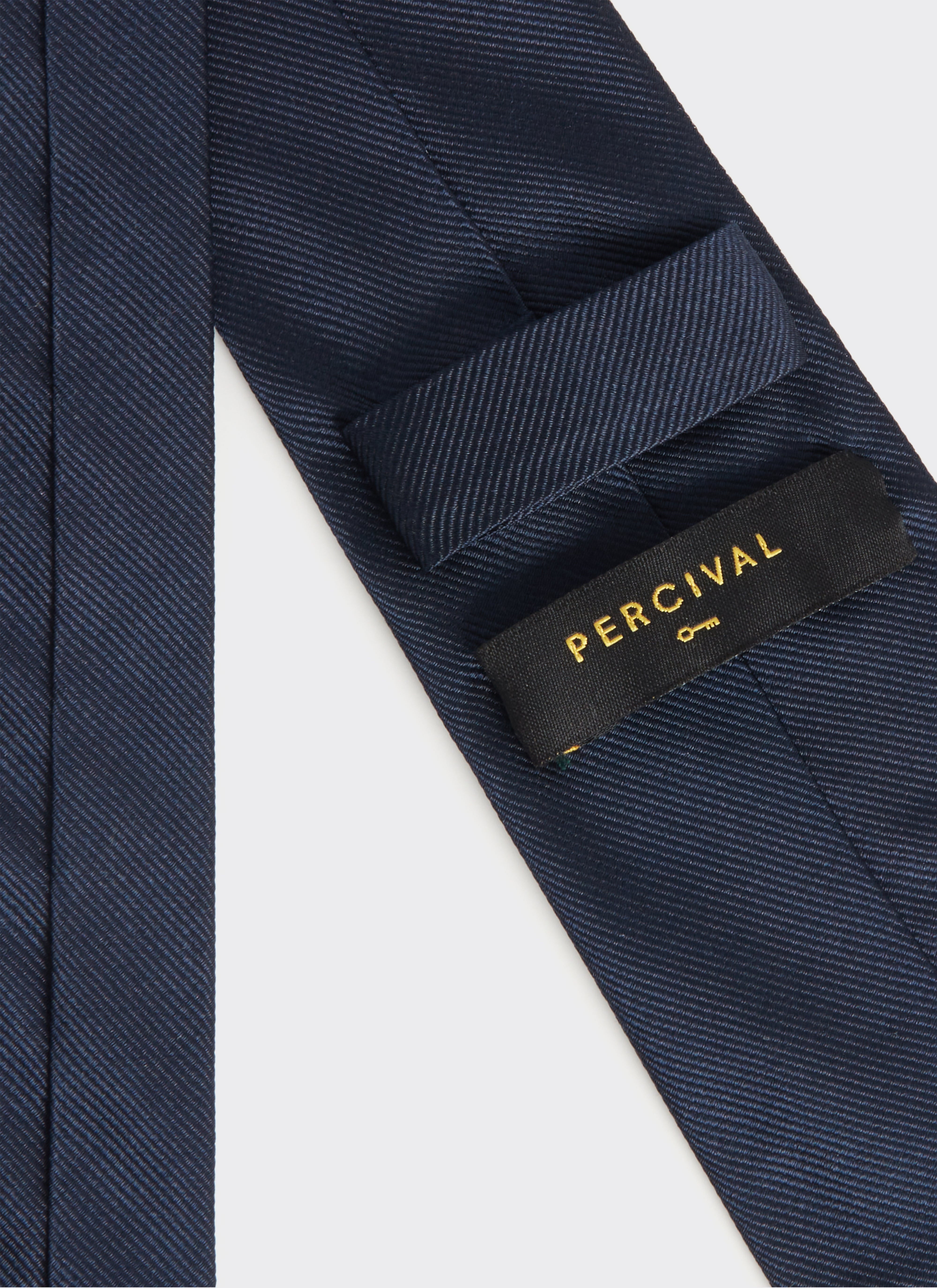 A close-up of the navy blue silk World Key Tie by Percival, showing the black and gold label on the reverse.
