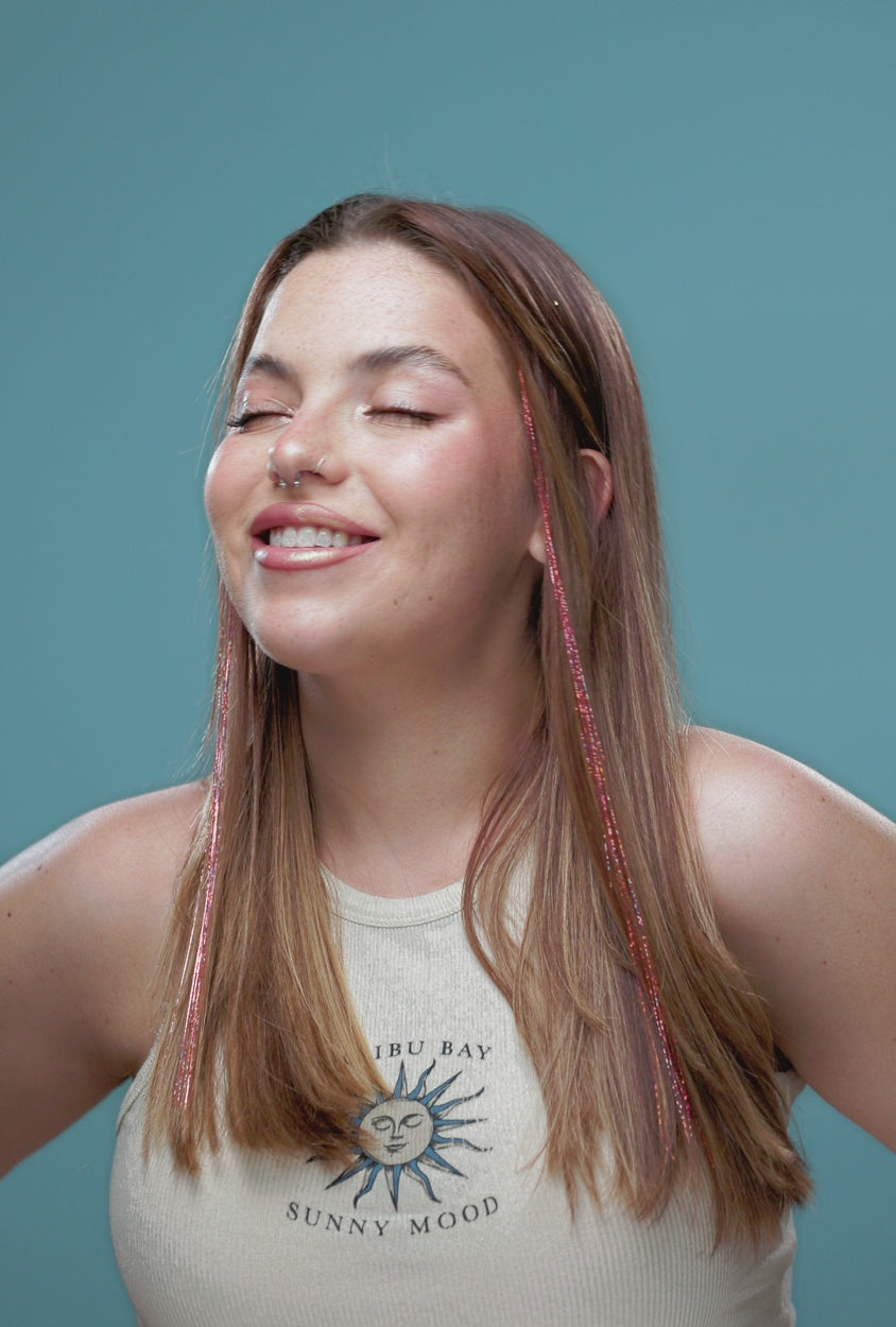 סרטון של בחורה שבשיער שלה שזורים חוטי טינסל בצבעי ורוד עתיק זוהר - הנקראים אצלנו גווני פיות. מיועדים לחיבור עצמאי, פשוט וקבוע לשיער או לחיבור זמני - Shufizoo