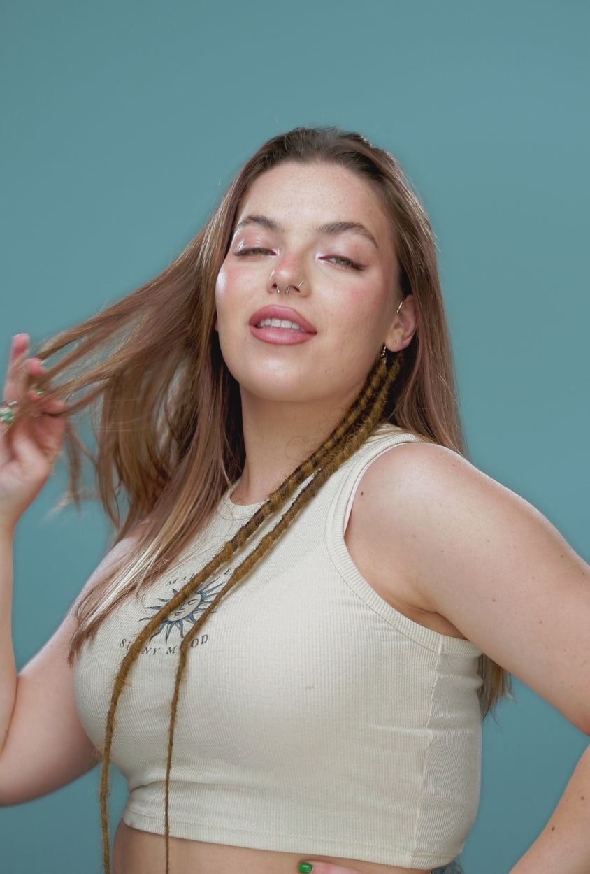 סרטון של בחורה עם שיער חום בהיר שהיא עונדת על האוזן תכשיט אוזן מקושט ראסטות. ביד היא שופכת חרוזי ראסטות ואז משחילה אותם על הראסטות הסינטטיות - Shufizoo 