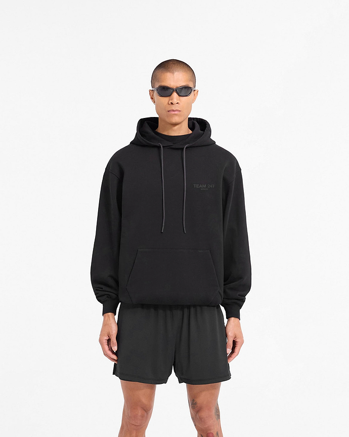 Man wearing an oversized black hoodie on a plain white background | Team 247 Oversized Hoodie in Matte Black | Oversized fit hoodie with matte black print | 247 Hoodies | Represent Clo