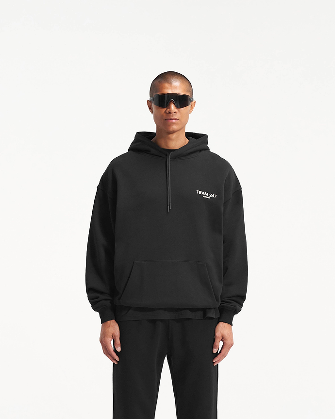 Man wearing a black oversized hoodie on a plain white background | Team 247 Oversized Hoodie in Black | Oversized hoodie with ribbed cuffs and Team 247 print | 247 Hoodies | Represent Clo