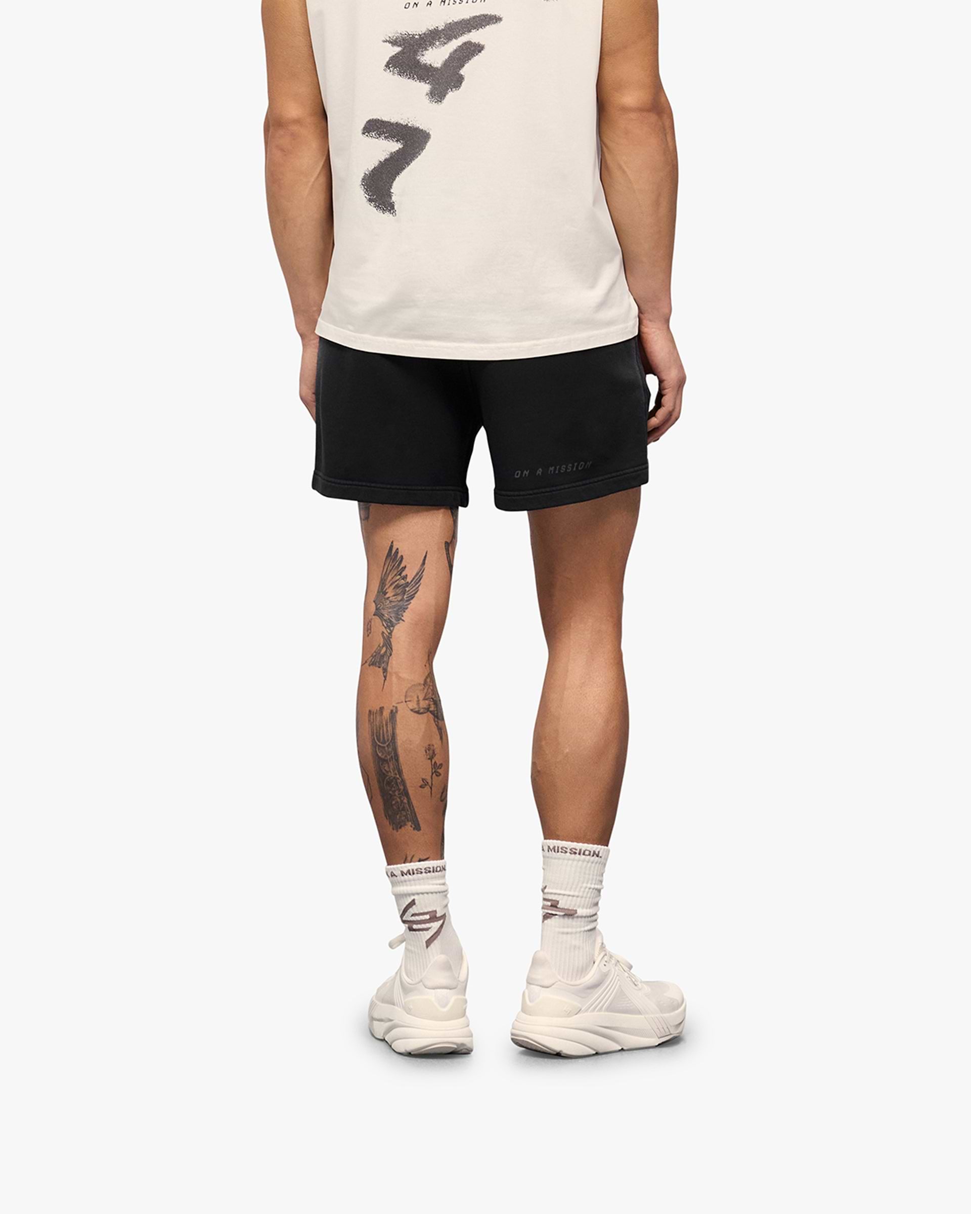 Man wearing aged black shorts on a plain white background | 247 Motion Shorts in Aged Black | Shorts with elasticated waistband and graphic print | 247 Shorts | Represent Clo