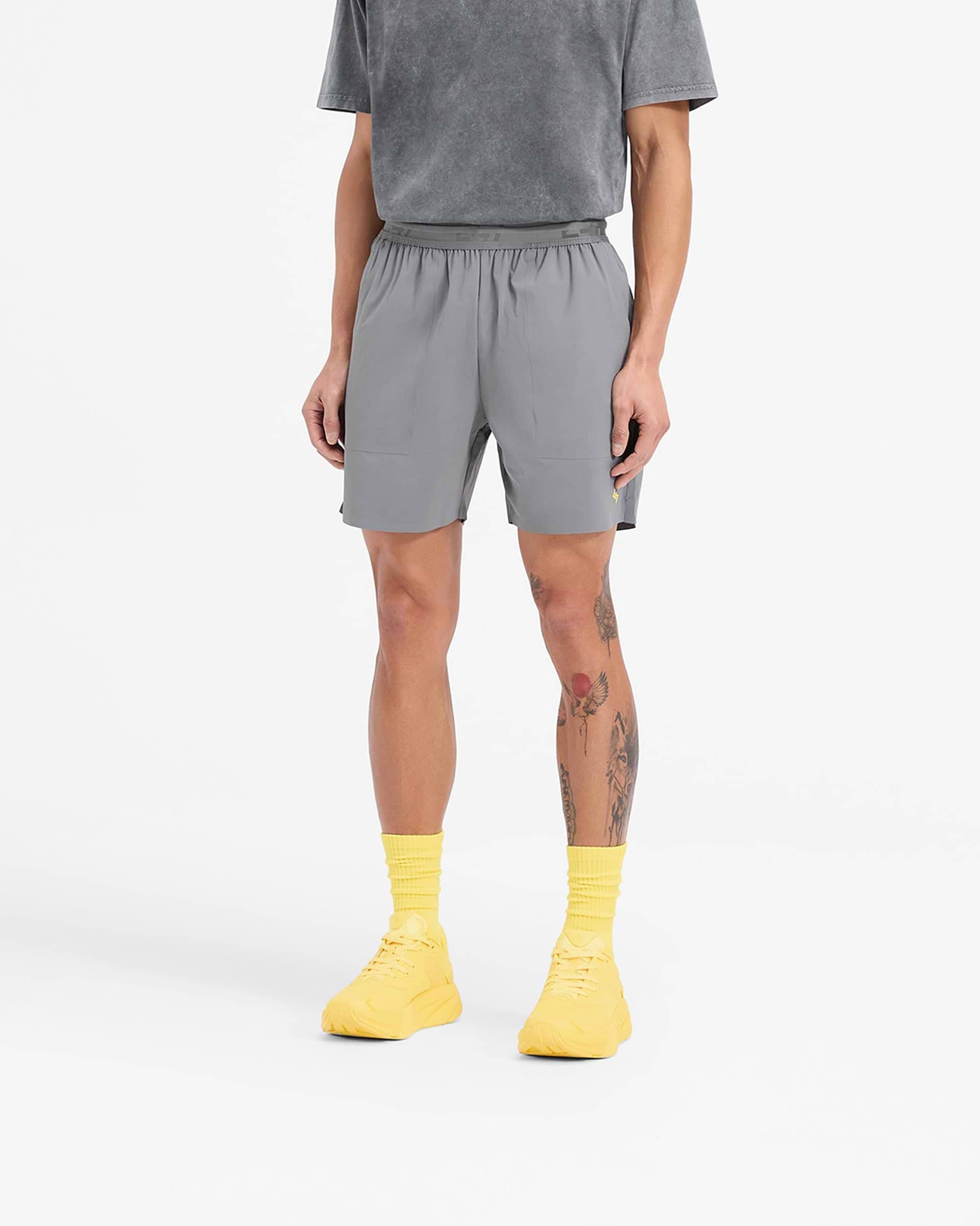 Man wearing grey shorts with yellow accents on a plain white background | Team 247 Fused Shorts in Pewter Lemon | Durable gym shorts with 4 way stretch and quick drying features | 247 Shorts | Represent Clo