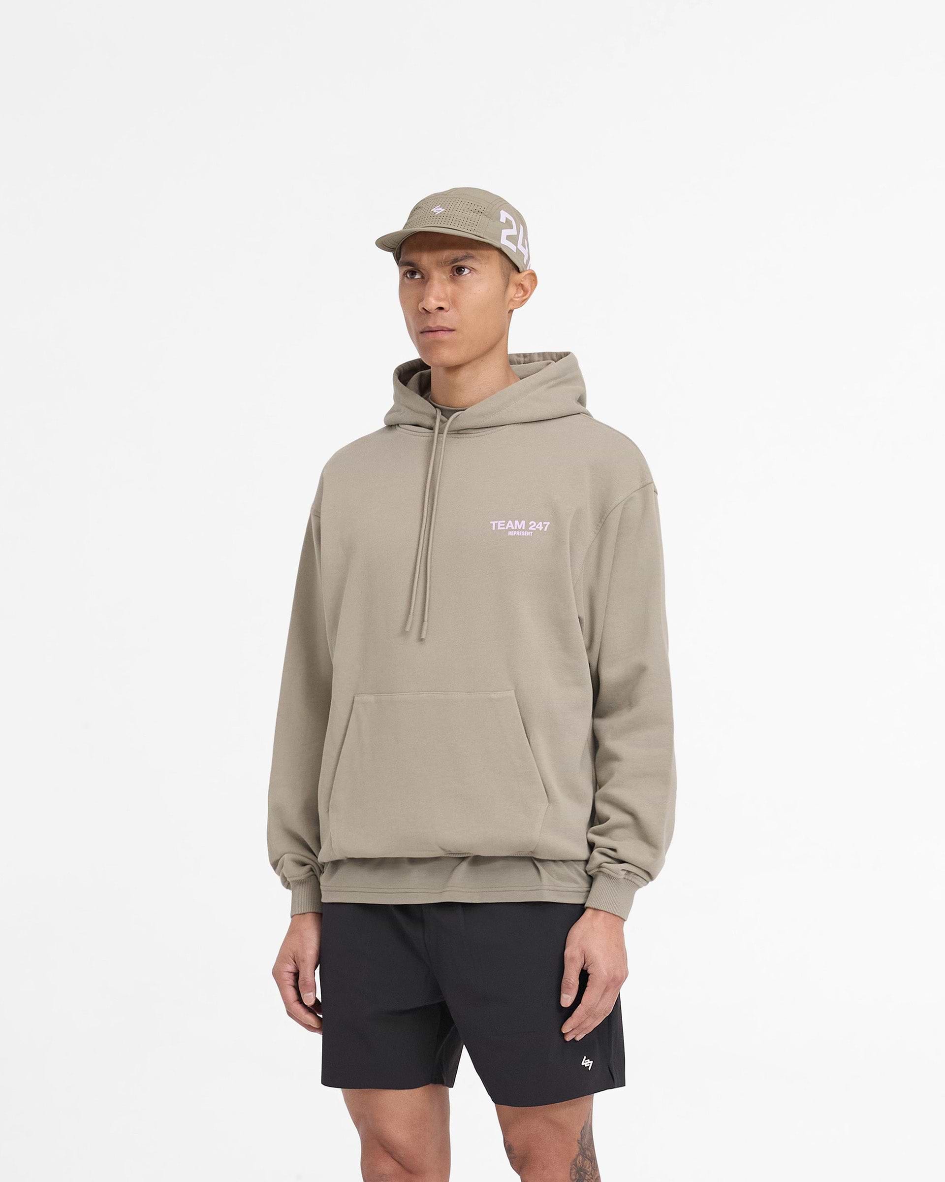 Man wearing a khaki hoodie with lilac accents on a plain white background | Team 247 Oversized Hoodie in Khaki Lilac | Oversized heavyweight cotton hoodie with Team 247 branding | 247 Hoodies | Represent Clo