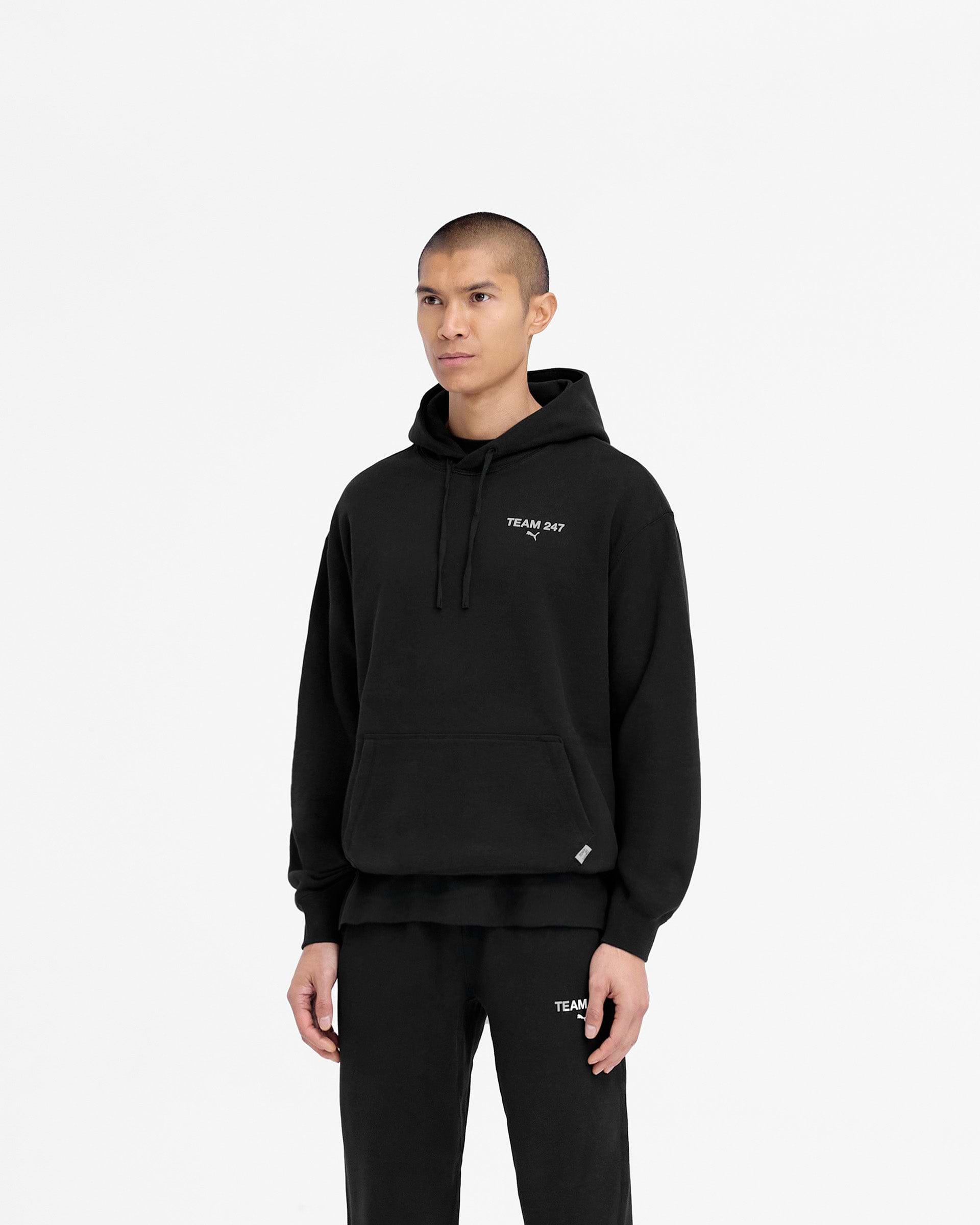 Man wearing a black hoodie on a plain white background | 247 X Puma Hoodie in Black | Relaxed fit hoodie with 3D silicon branding and adjustable drawcord | 247 Hoodies | Represent Clo
