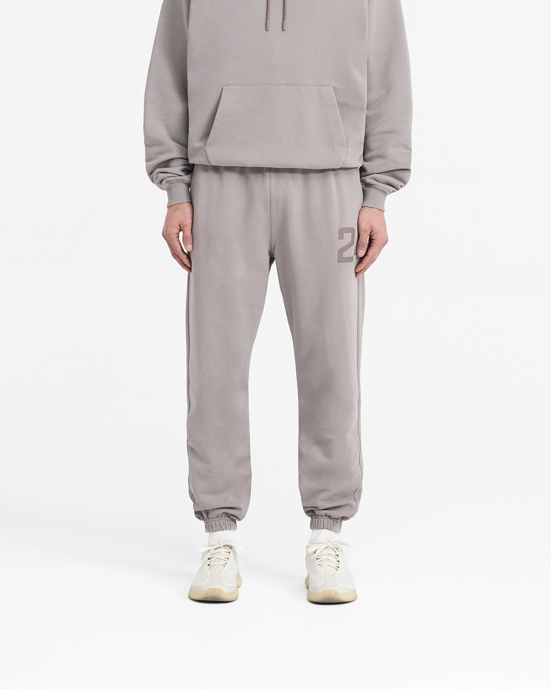 Man wearing grey sweatpants on a plain white background | 247 Sweatpant in Cinder | Joggers with elasticated cuffs & drawcord waistband | 247 Pants | Represent Clo