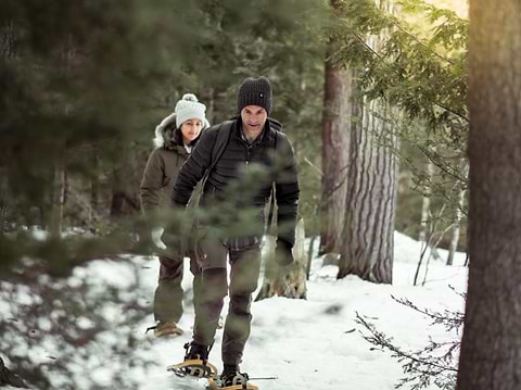 Man and woman wearing warm Heat Holders® gear, snowshoe in the woods.