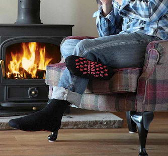A man wears Heat Holders® slipper socks while sitting near a fire.