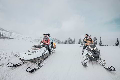 Four people riding on two snowmobiles