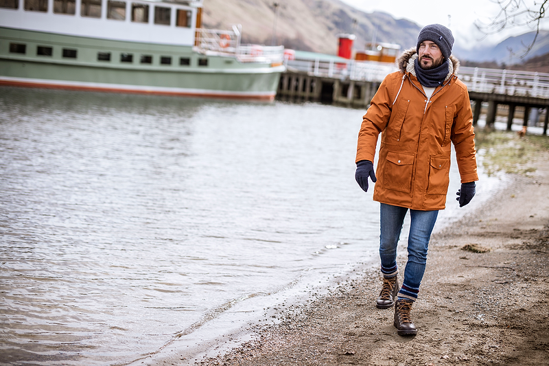 Man walks along a river in winter, wearing a winter coat, hat and gloves. Heat Holders® Men's thermal clothes for winter.