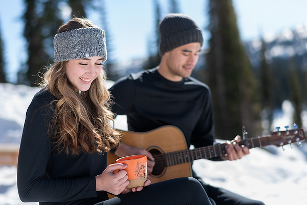 Couple sitting outside in the winter. He is playing guitar and she is drinking cocoa