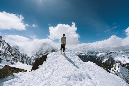 Essential Gear for Preparing for Winter - Man stands on a mountain peak looking at the mountains around him. | Heat Holders®